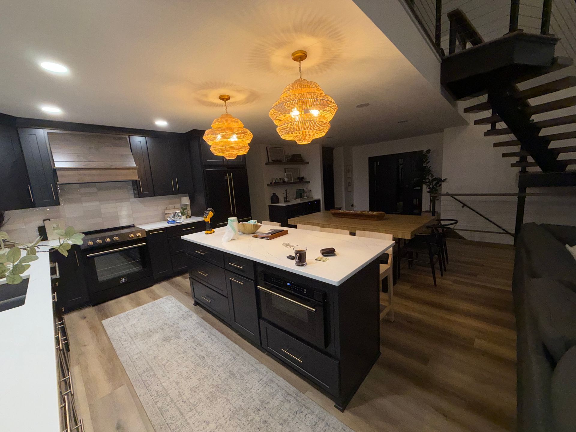 Modern kitchen and dining area with dark cabinets, white island, warm pendant lights, and staircase nearby