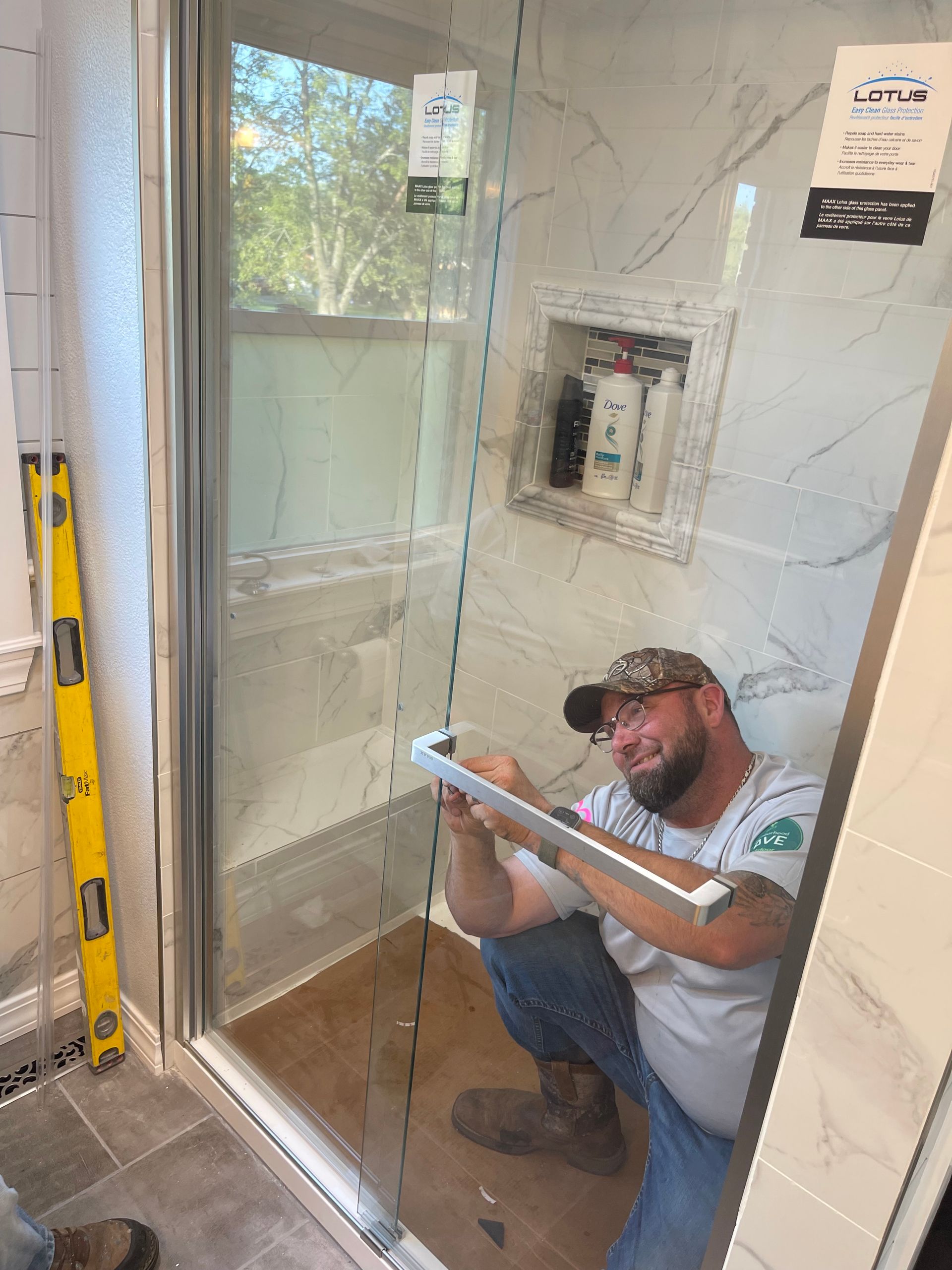 Worker sitting in a shower stall, inspecting a glass door and tile wall in a bathroom.