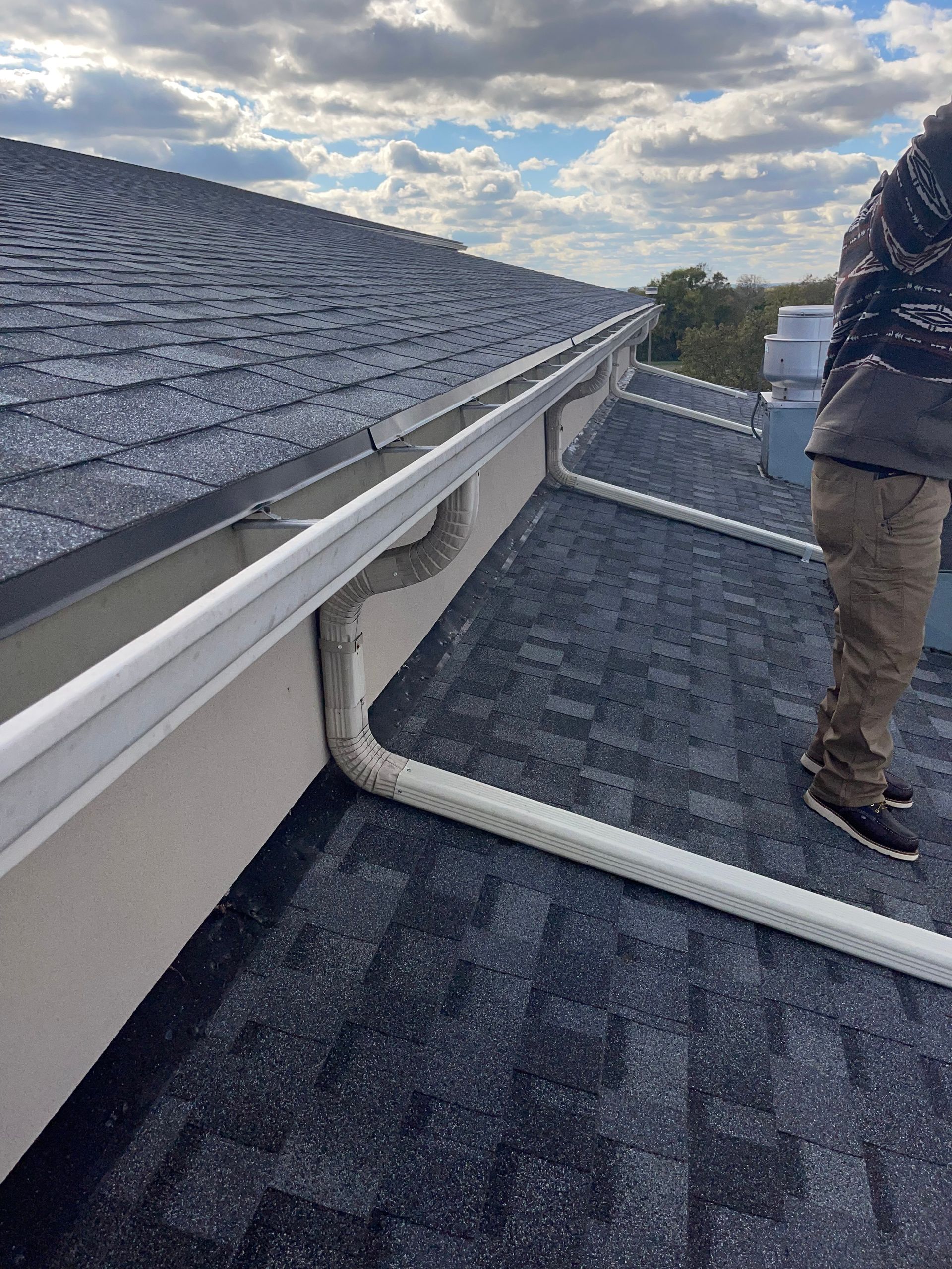 Roofers inspecting dark shingle roof and white gutter on a sloped residential roof at dusk