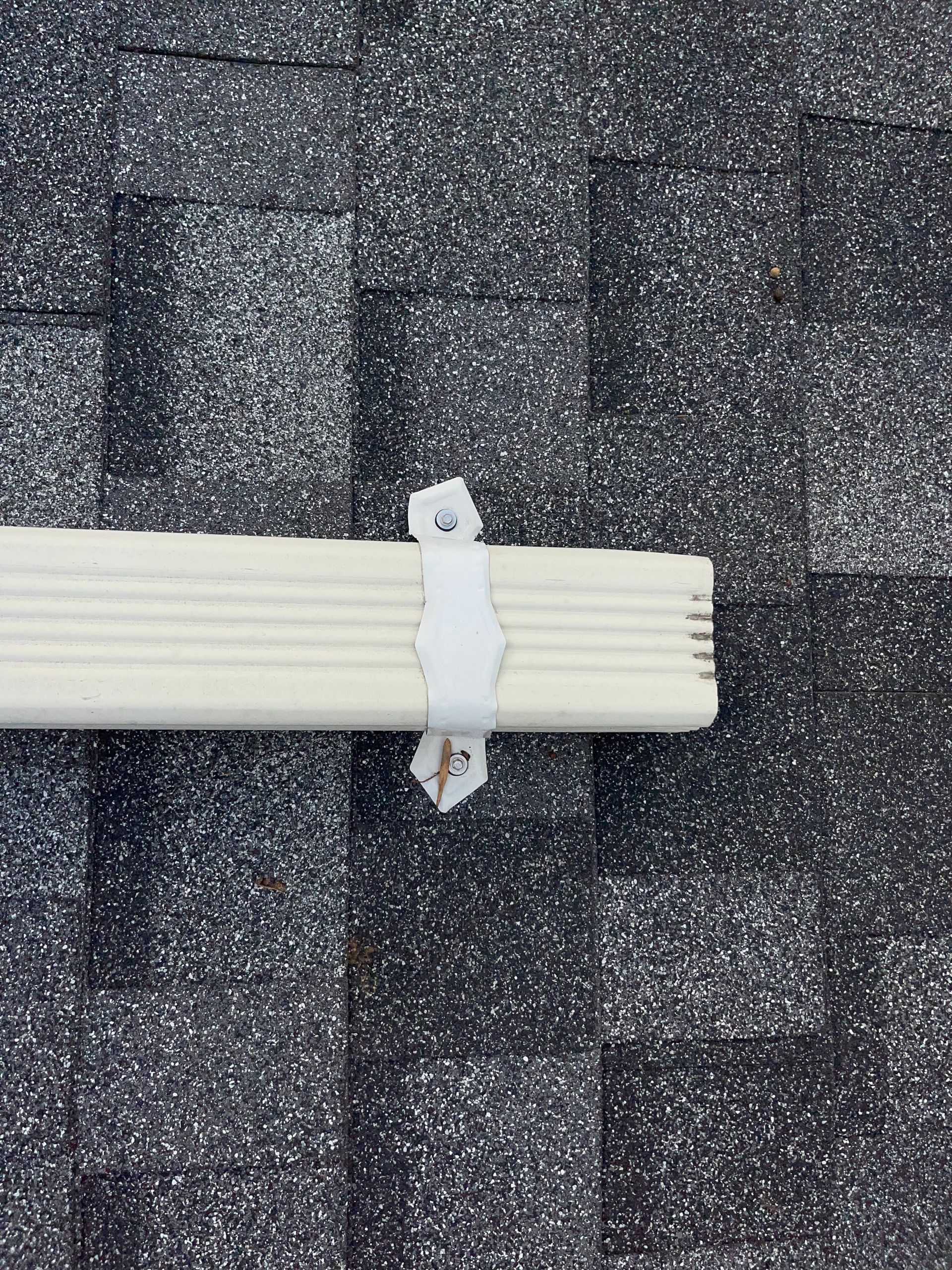 Bundle of white cables strapped to a dark roof shingle surface with tape