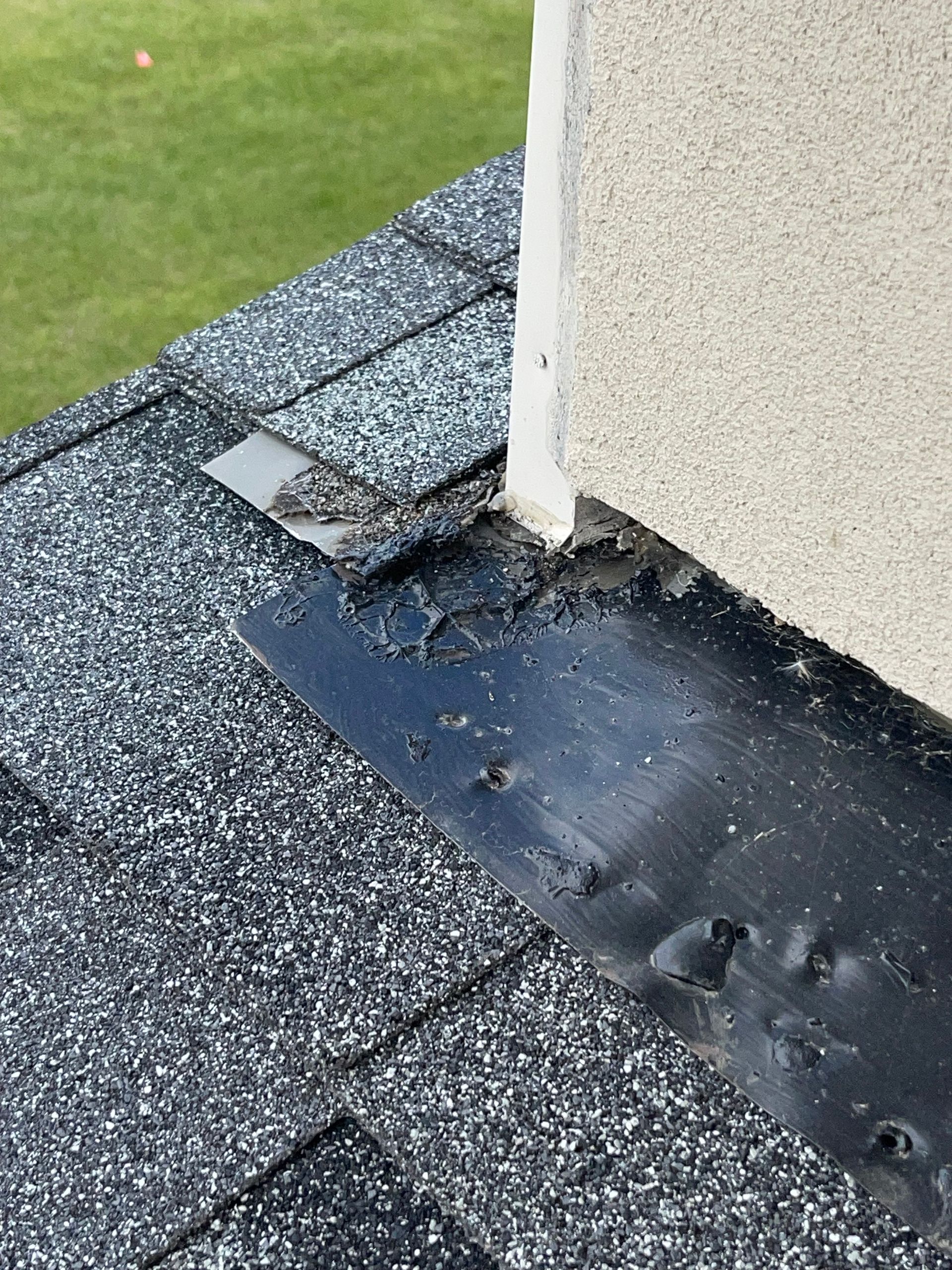Damaged roof flashing around a white post, with torn shingles and exposed black membrane.