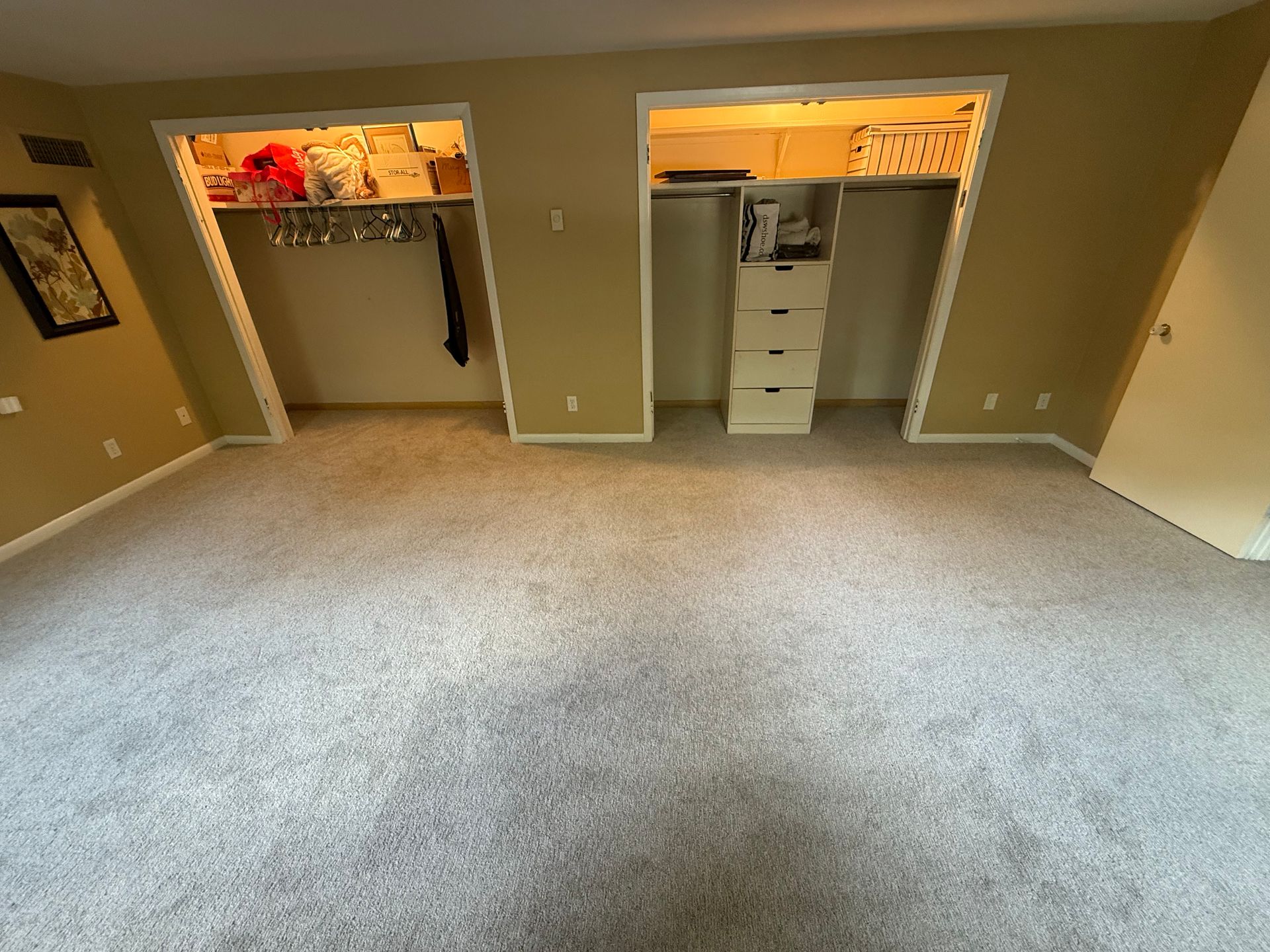Empty beige carpeted bedroom with two open closets and a doorway on the left