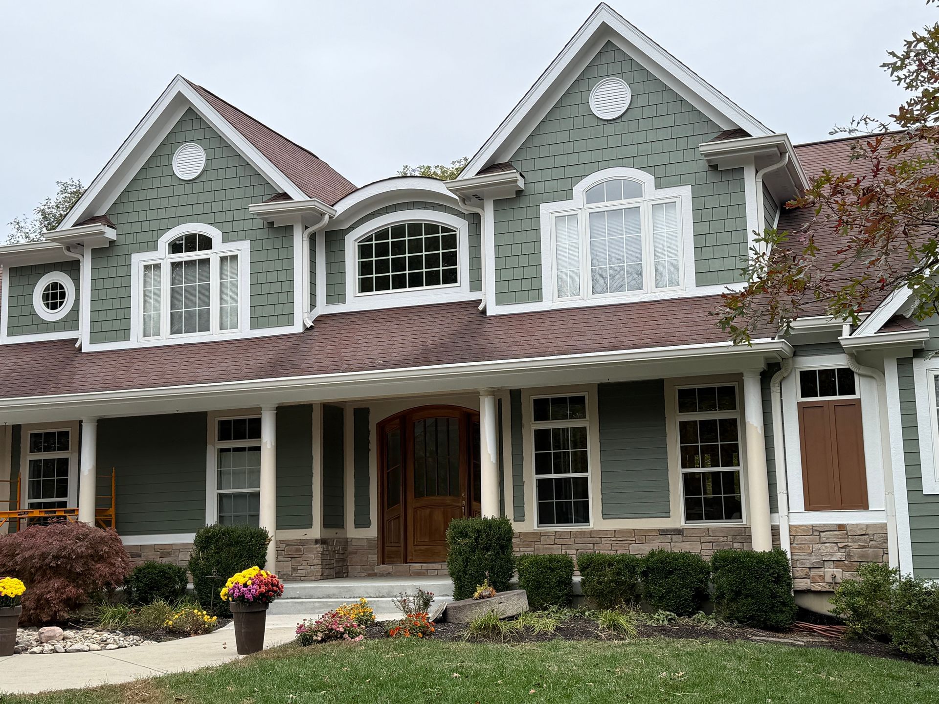 Row of green and white townhomes with arched windows and a covered porch in front of landscaped shrubs