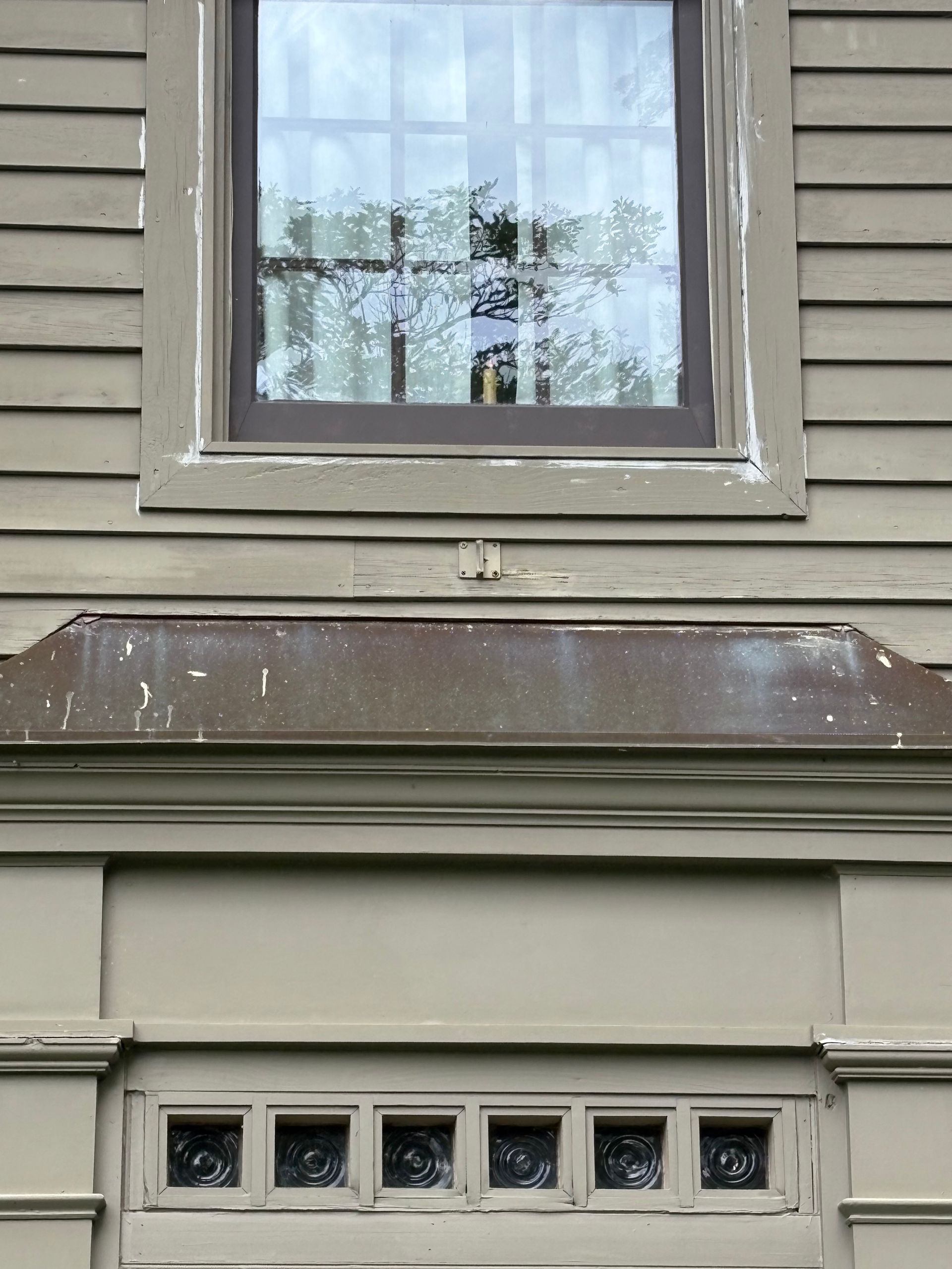 Weathered house exterior with a window above a brown awning and small basement windows below