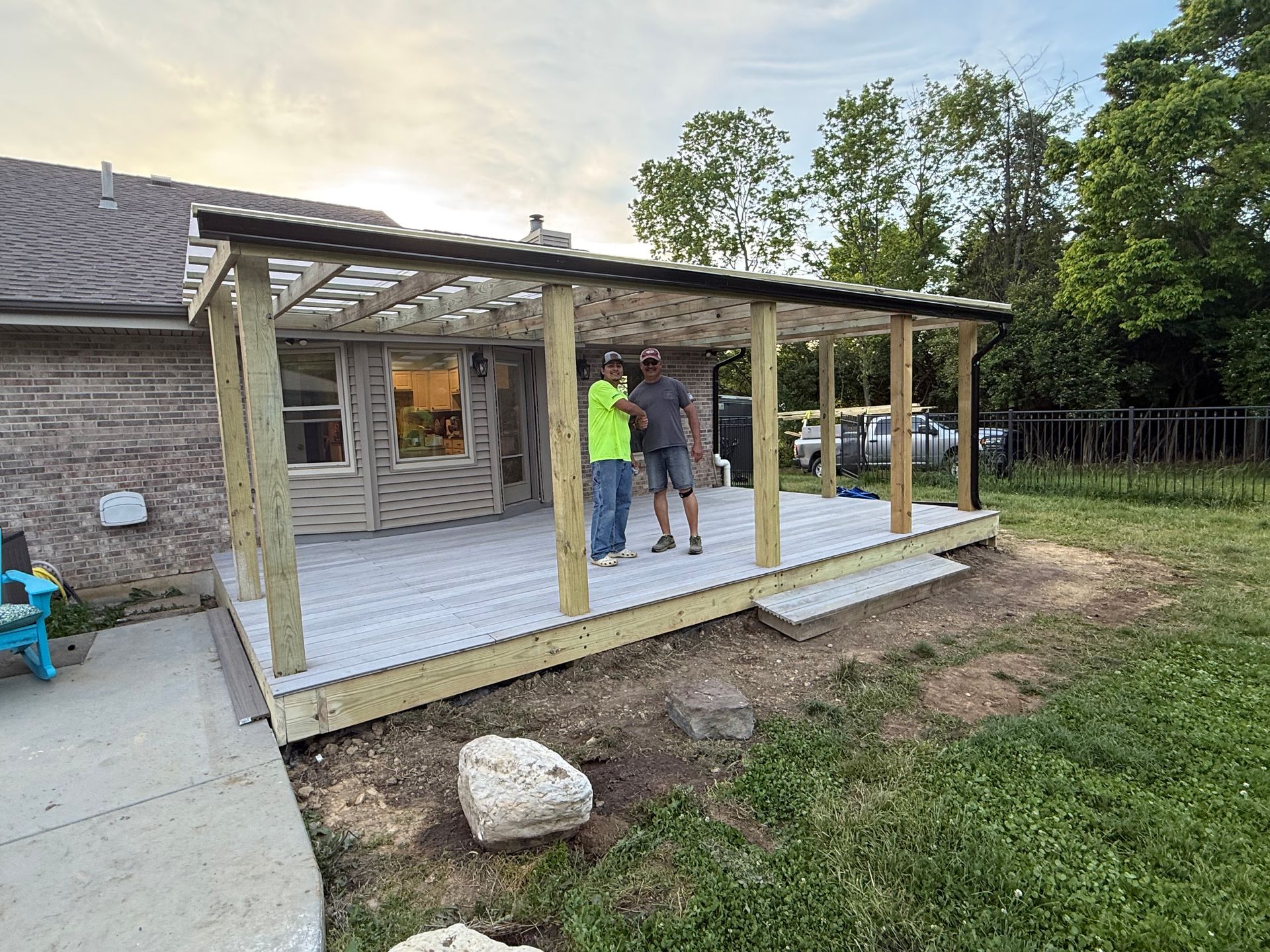 Partially built wooden porch/deck beside a house, with two workers standing on the new platform.