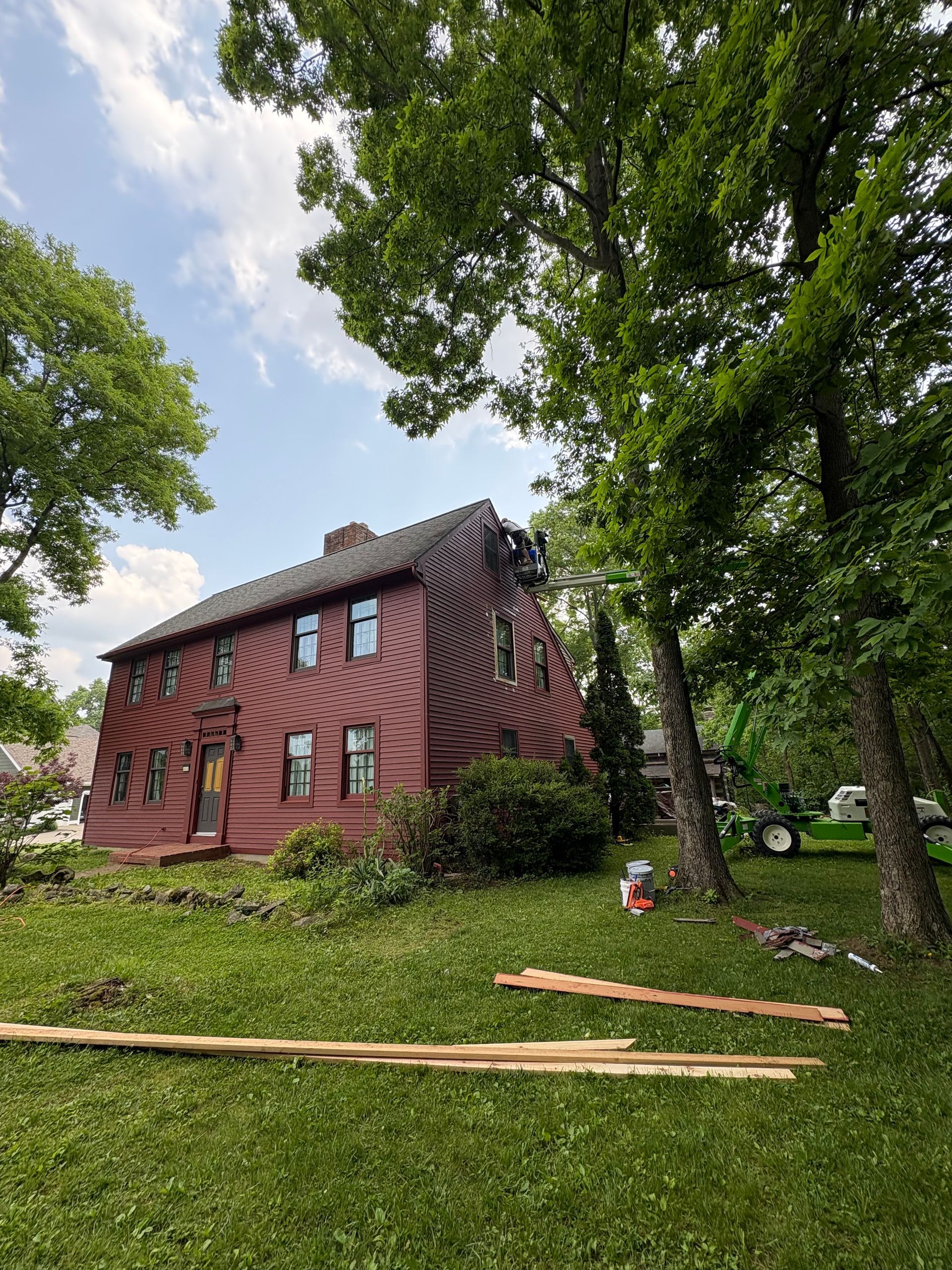 Red brick house with arched windows on a grassy hill, framed by tall green trees under a cloudy sky