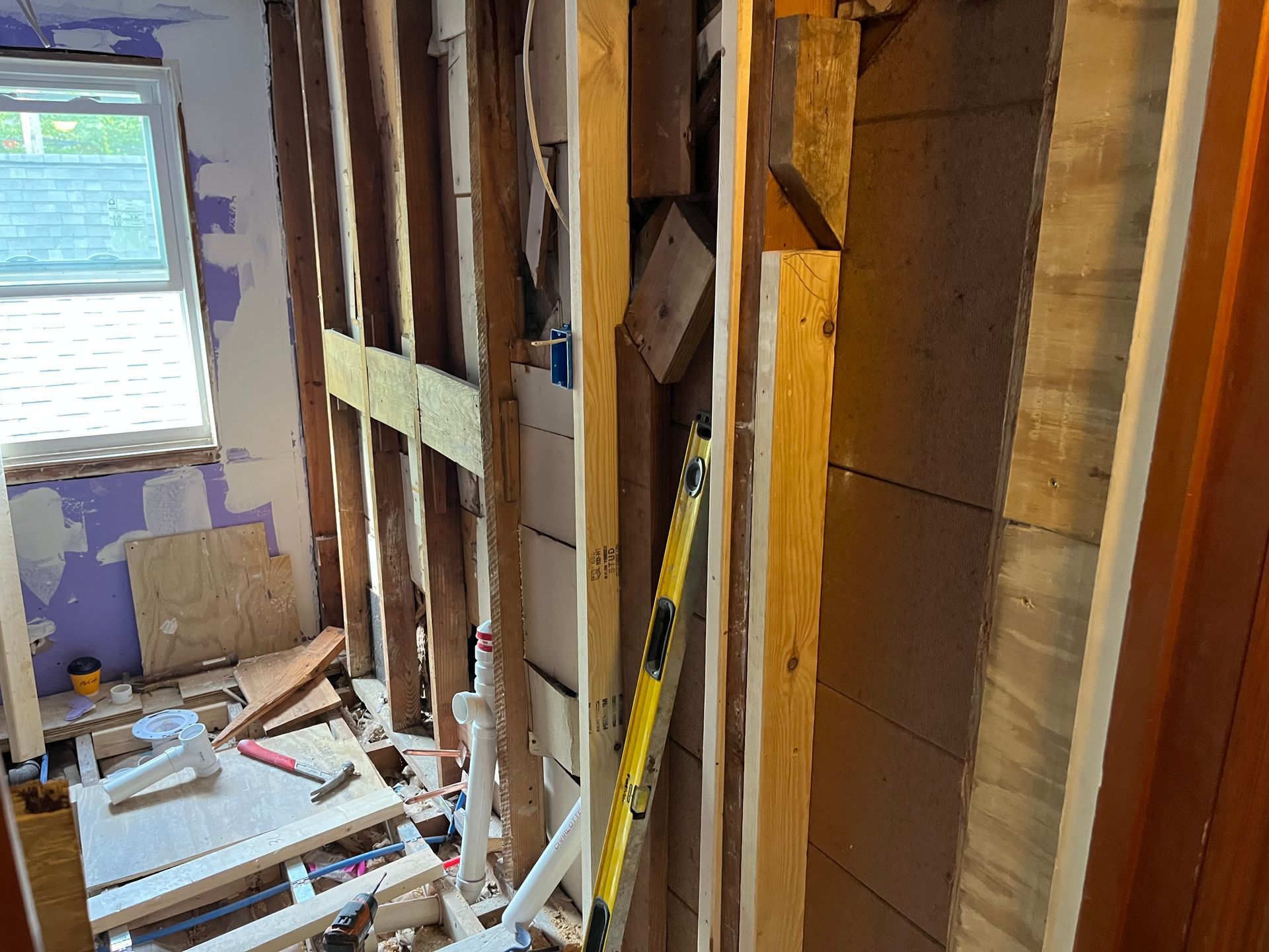 Partially demolished room with exposed studs, debris, and a yellow ladder near a window