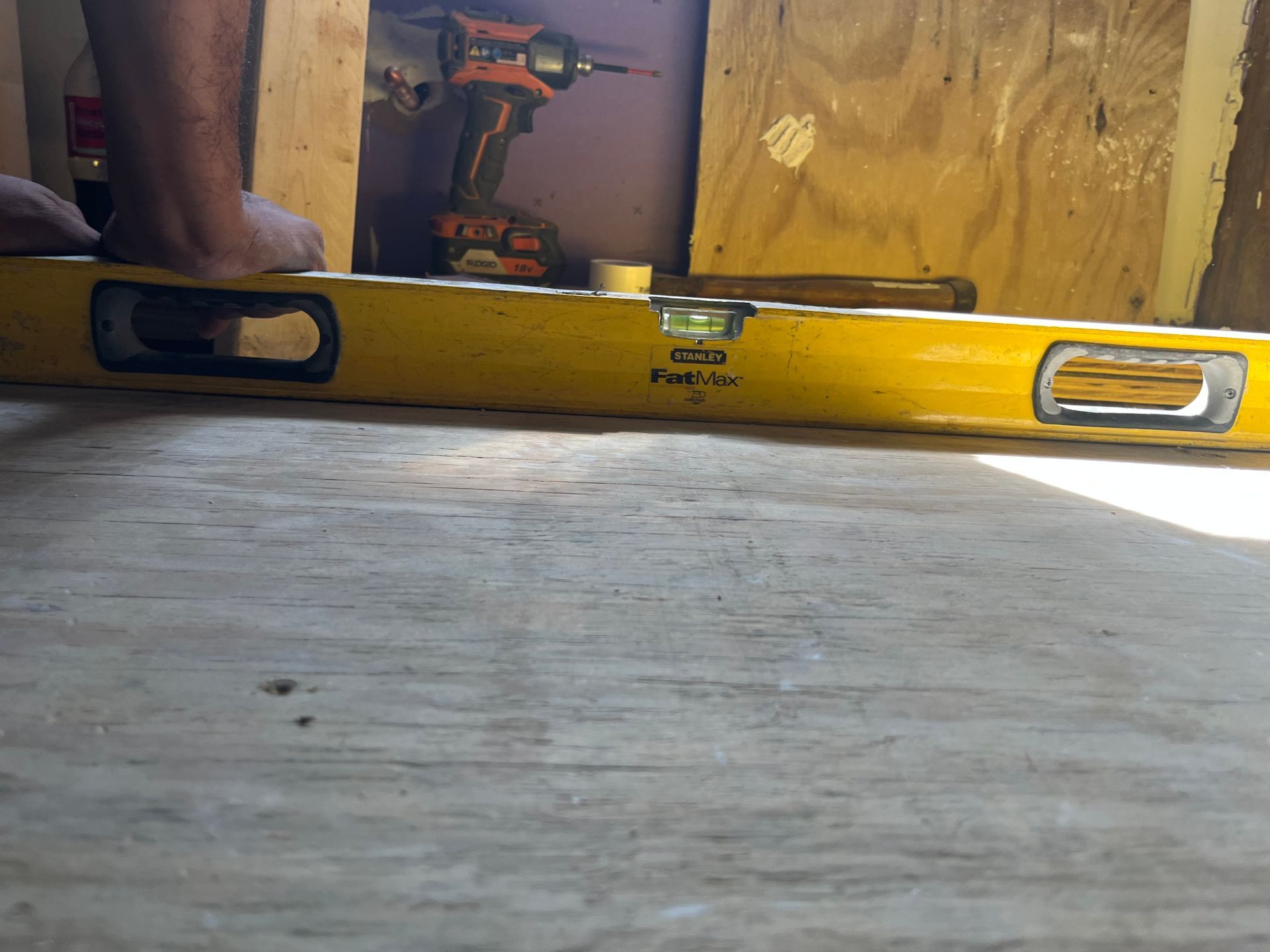 Yellow spirit level on floor with a drill and plywood in the background
