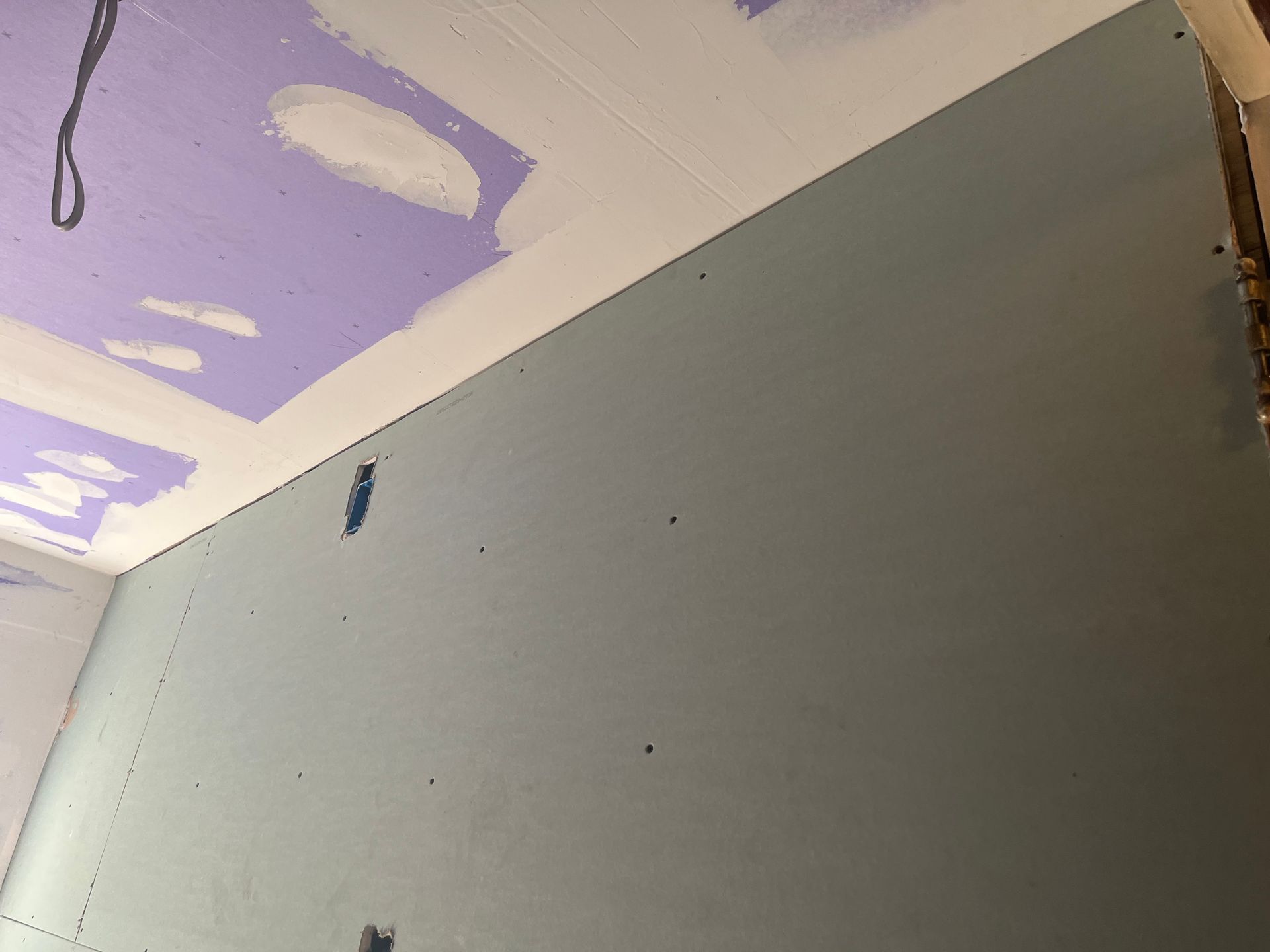 Partially painted wall and ceiling with purple patches and a gray wall panel being repaired
