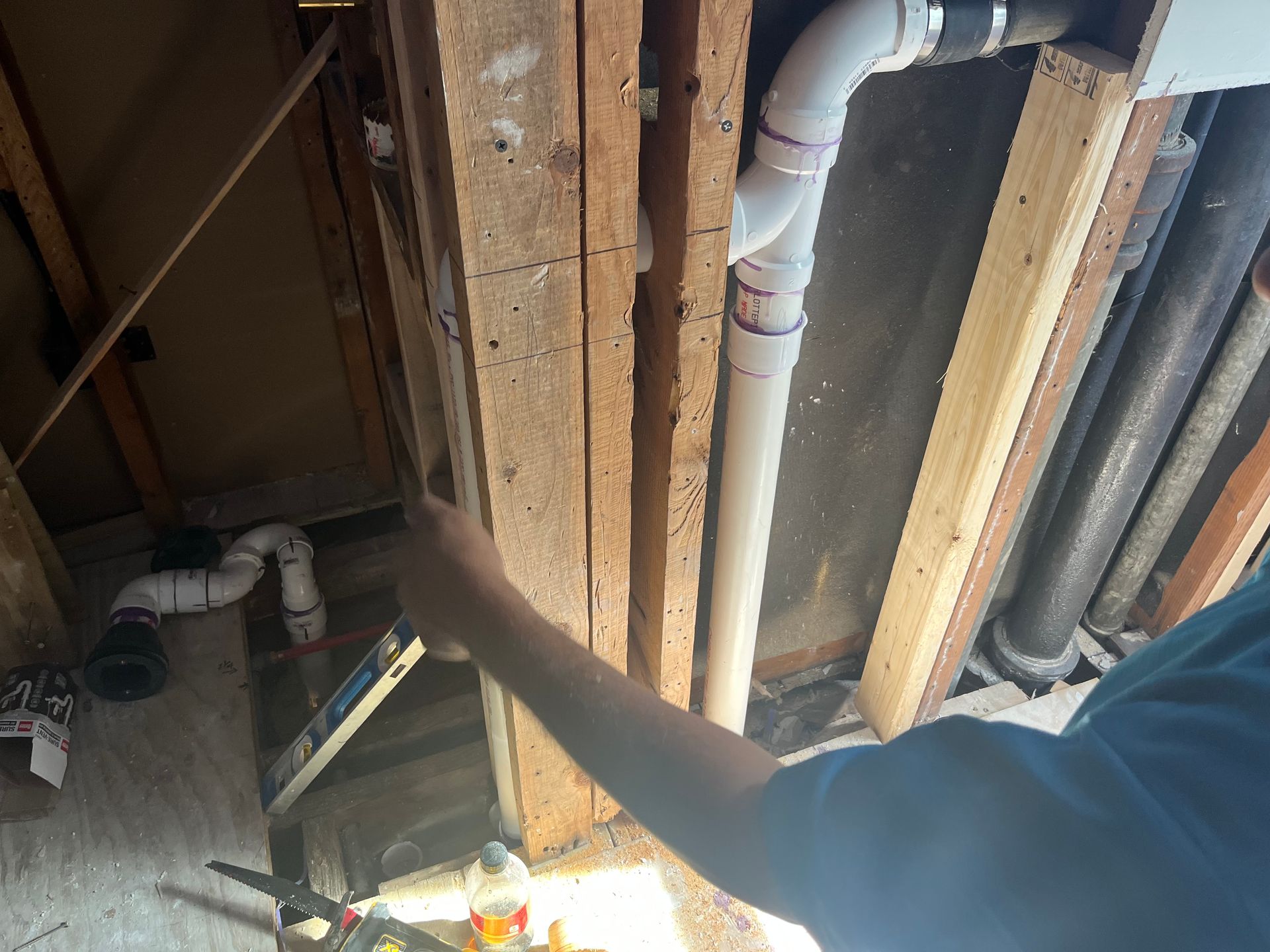 Arm reaching toward exposed ceiling joists and plumbing in a construction or repair area