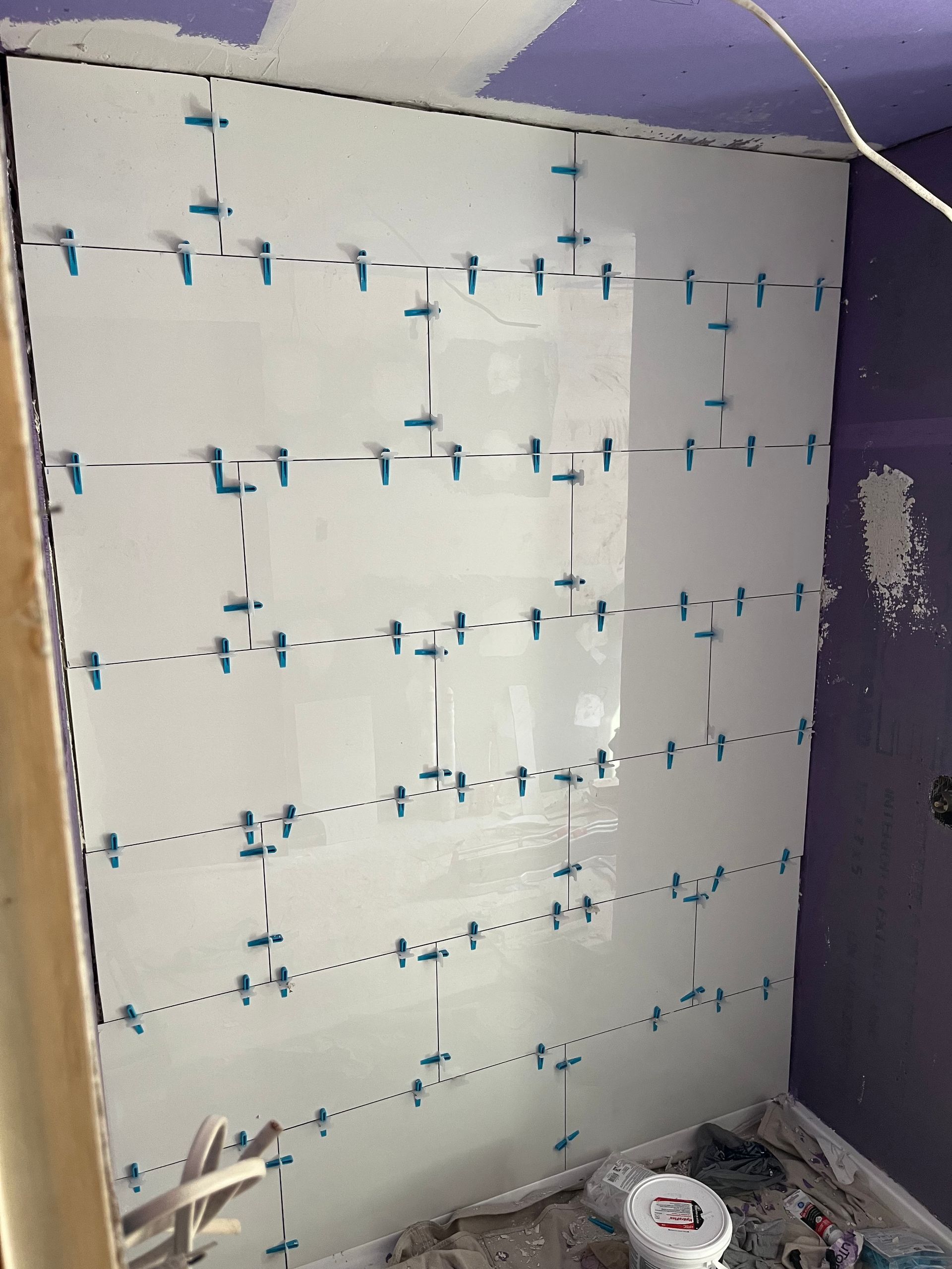 Partially tiled bathroom wall with blue spacers and tools on the floor during renovation
