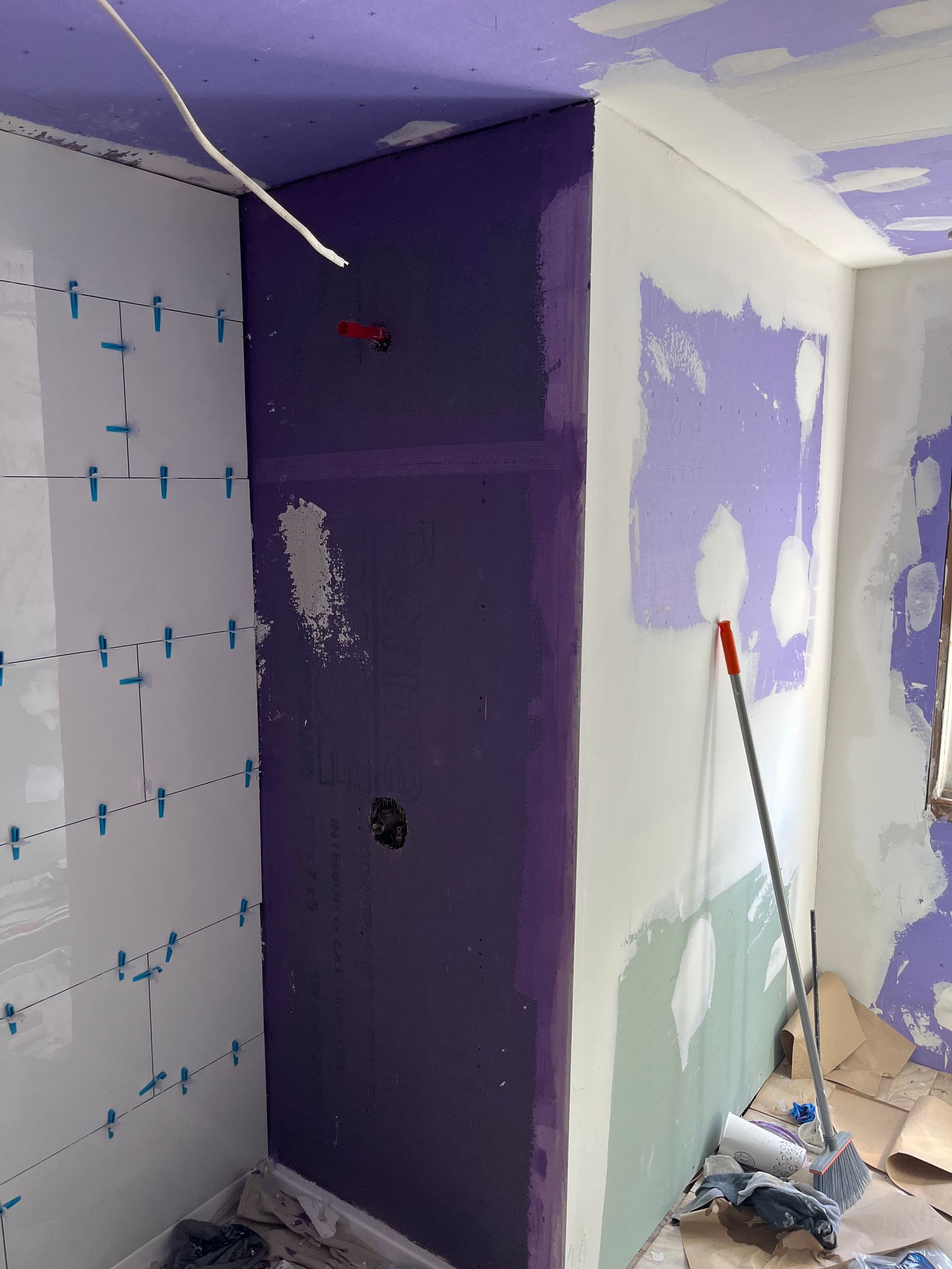 Partially renovated bathroom with purple and white walls, tile paneling, and cleaning tools on the floor