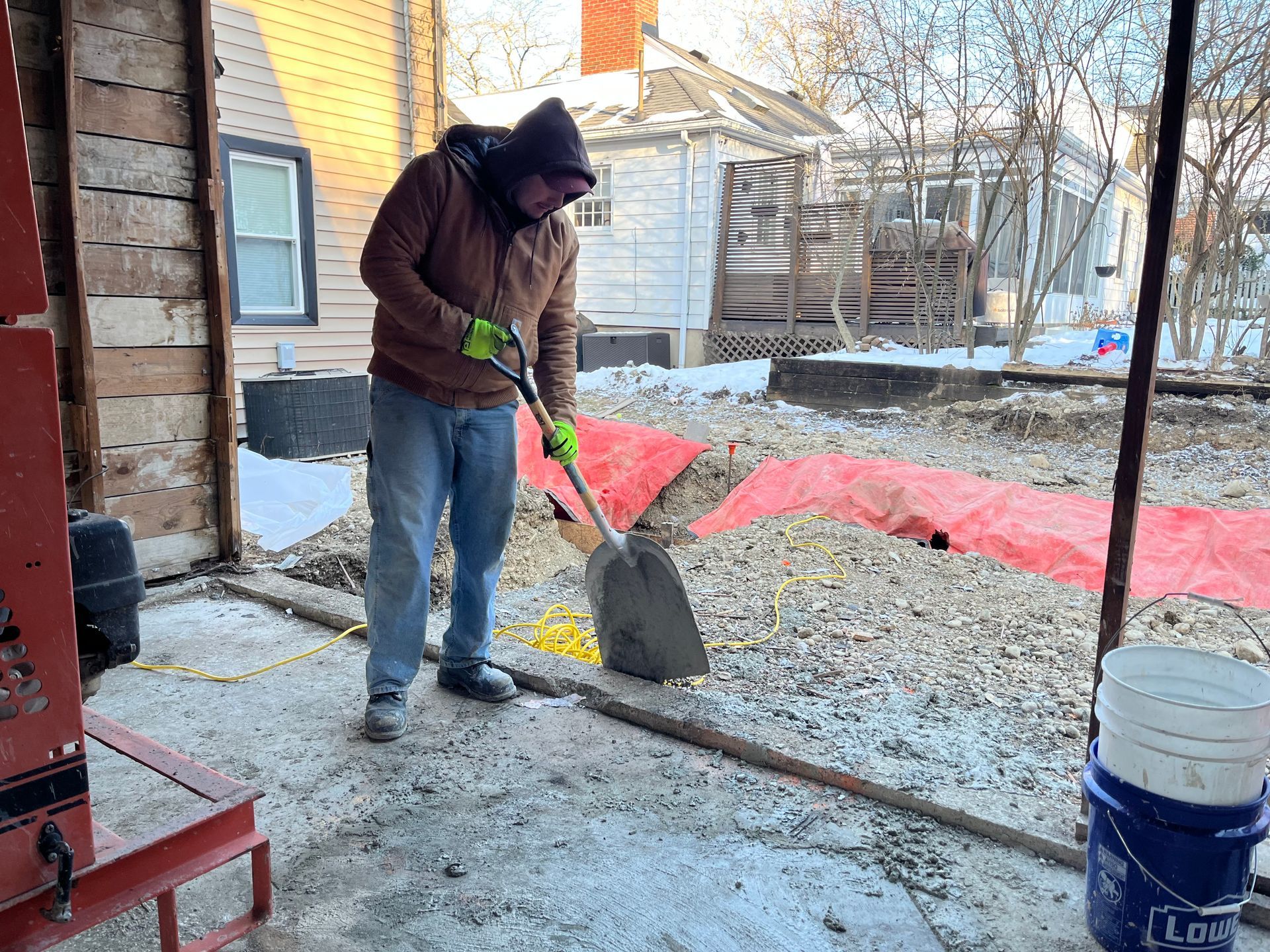 Person shoveling gravel in a snowy backyard beside a house