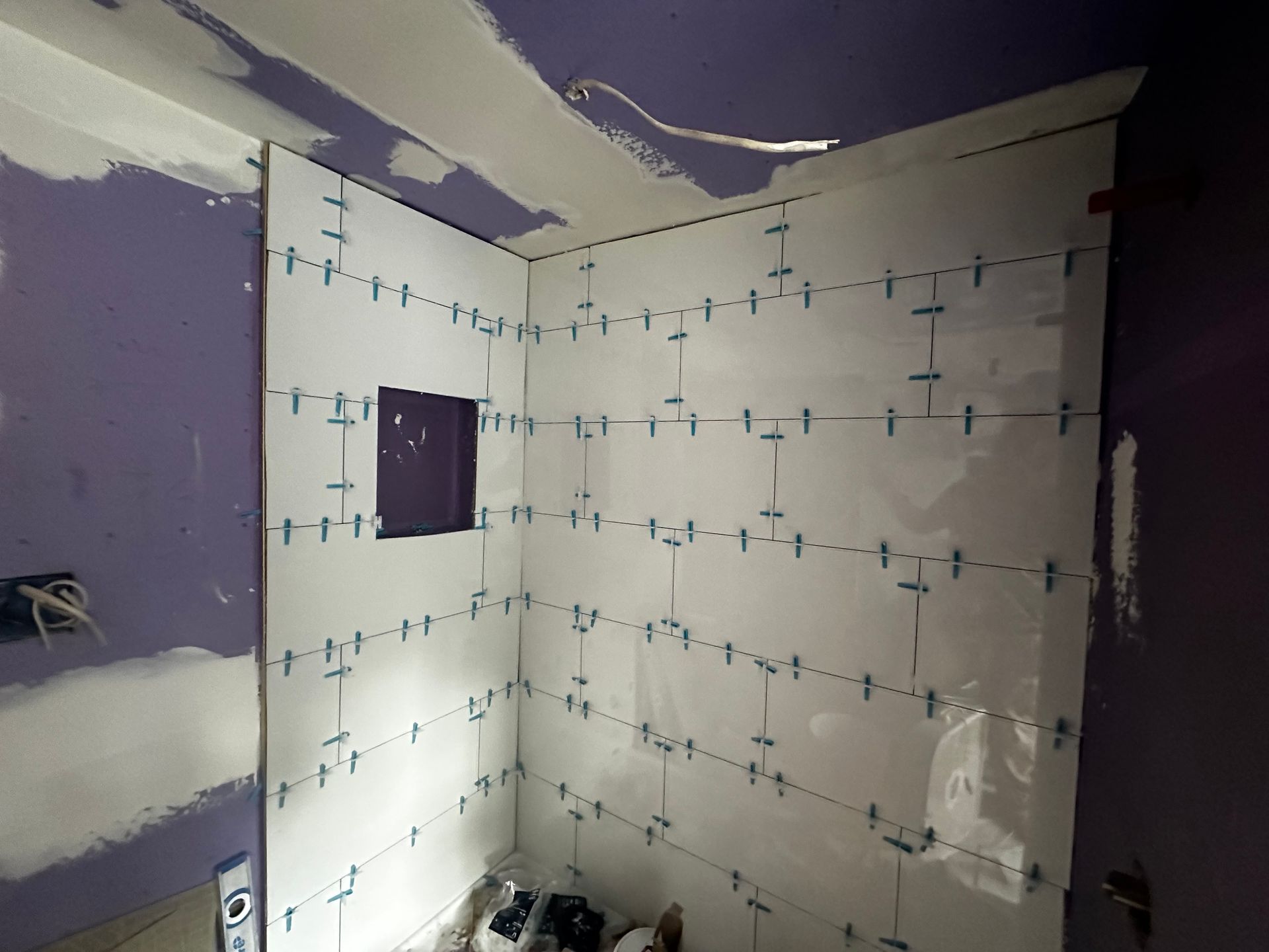 Partially tiled shower niche with white tiles and purple drywall during bathroom renovation