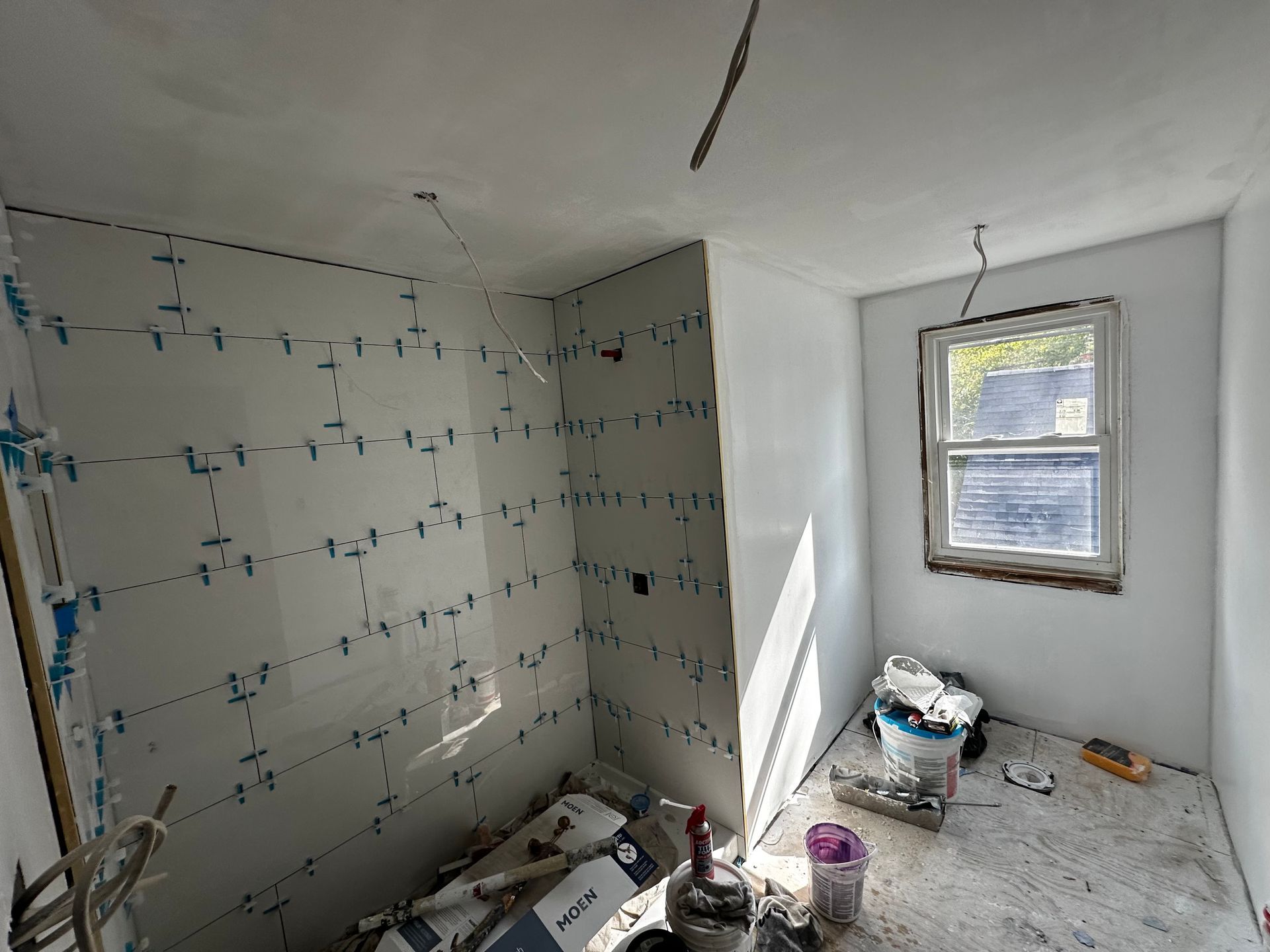 Small bathroom under renovation with tiled walls, scattered tools, and a window letting in daylight