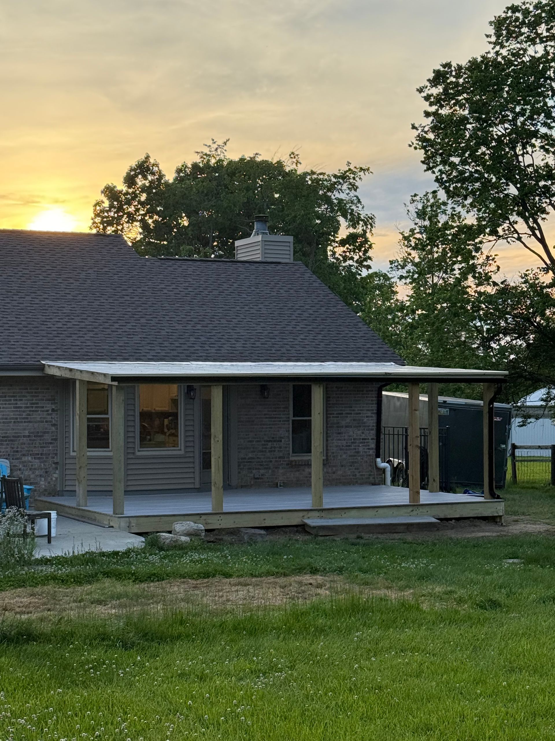Small brick house with a porch at sunset, framed by trees and a grassy yard.
