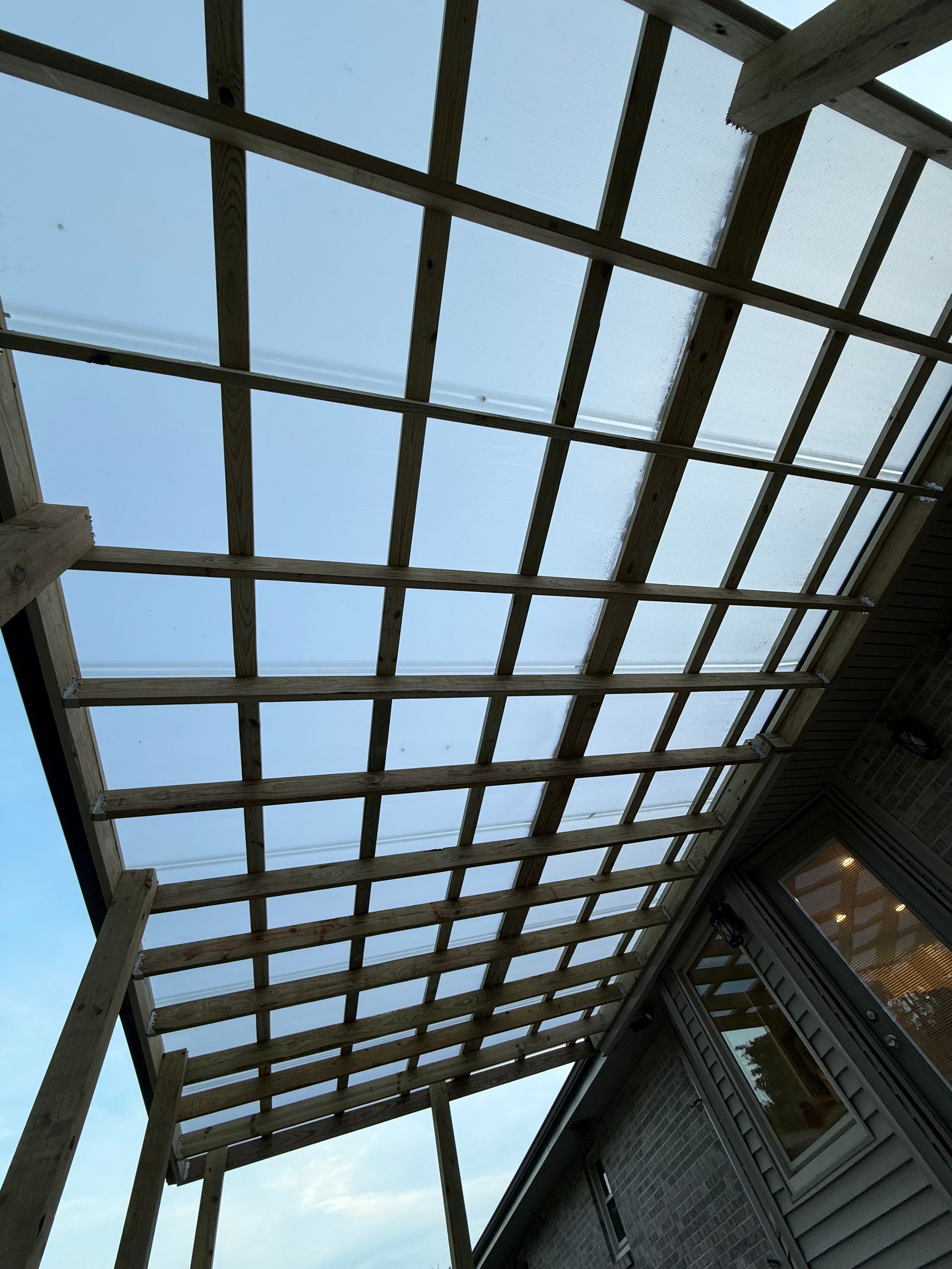 Glass roof with dark support beams over a brick building, viewed from below