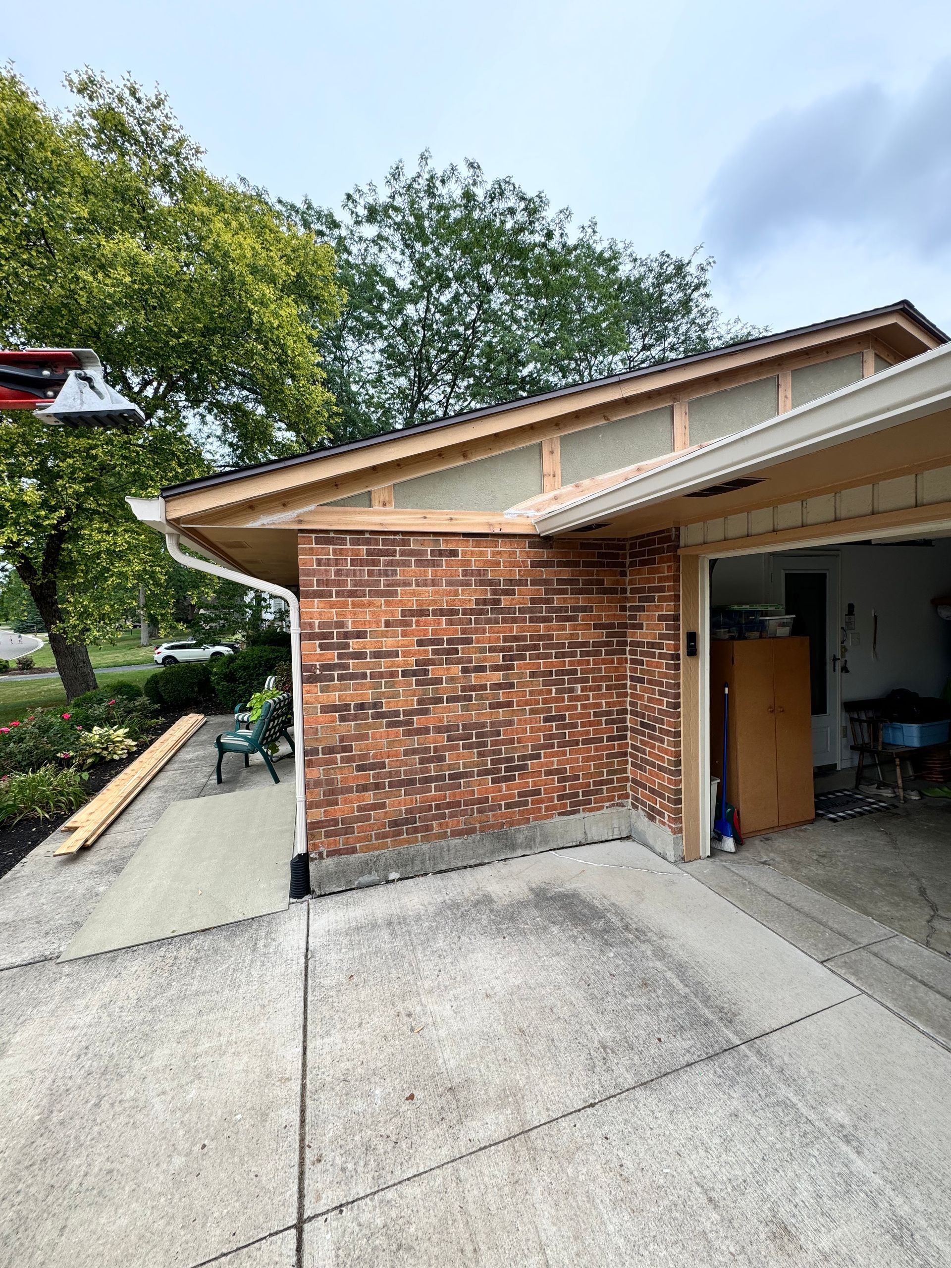 Brick house exterior with open garage and driveway, surrounded by trees