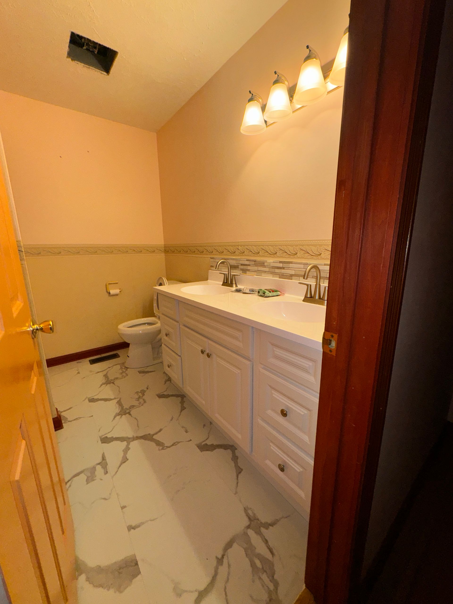 Small bathroom with white vanity, marble-style floor, toilet, and warm wall lighting.