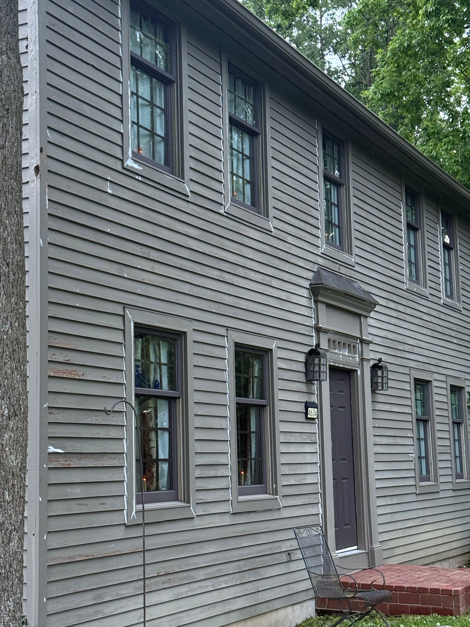 Gray wooden two-story house with shuttered windows and a red brick stoop
