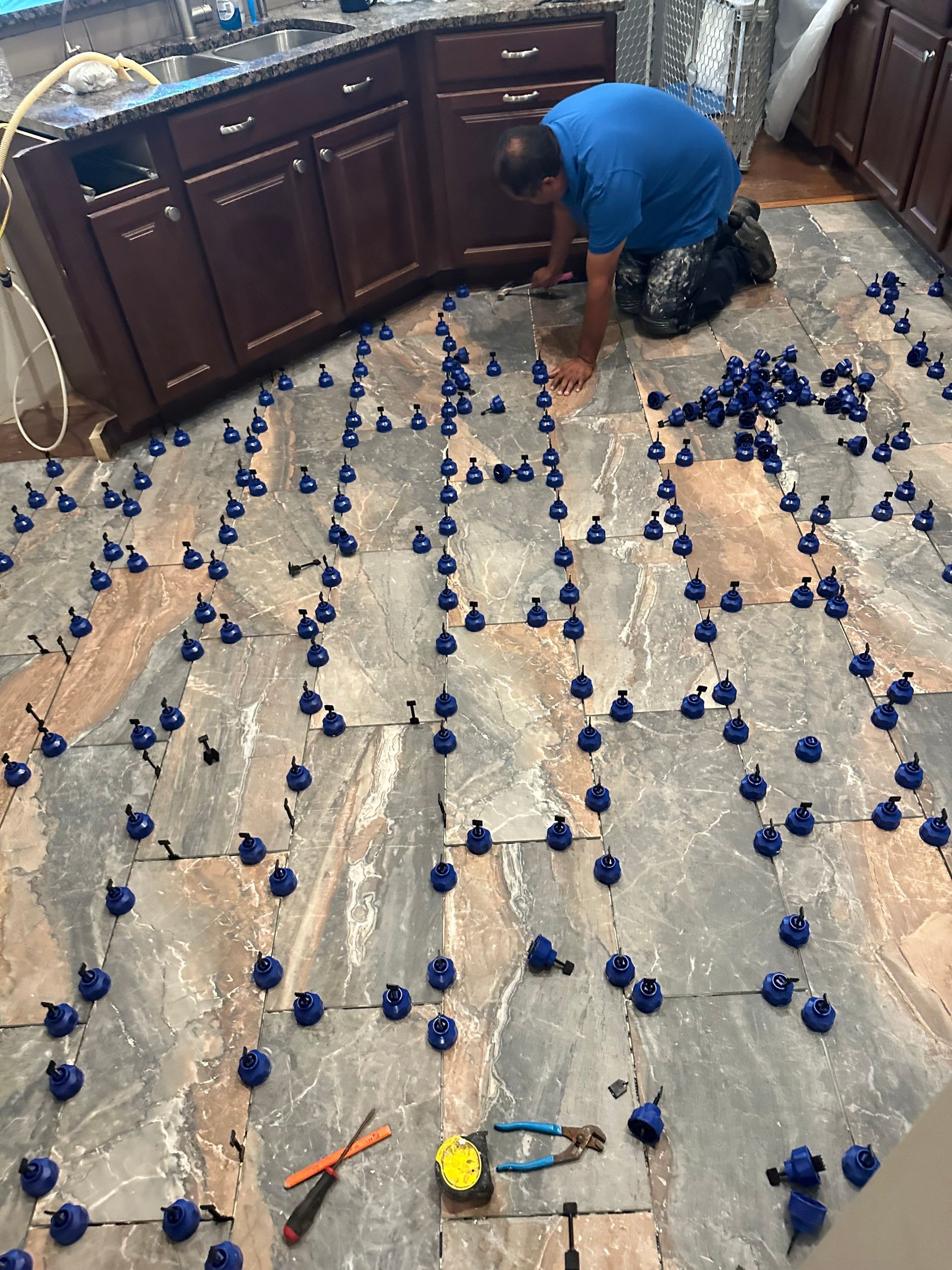 Person arranging blue flowers on a tarp-covered kitchen floor