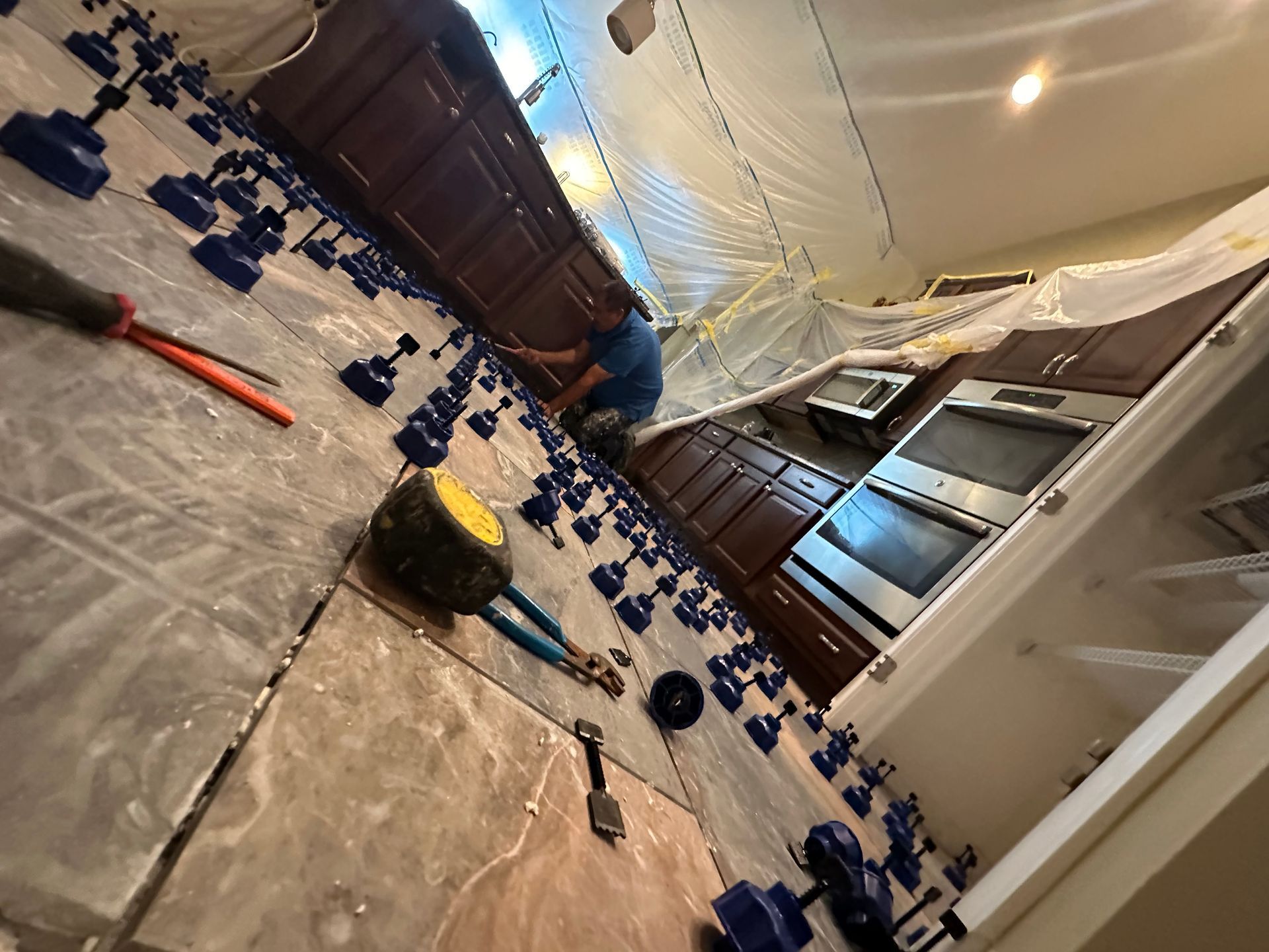 Low-angle view of a kitchen floor covered in scattered blue toy blocks and tools near cabinets and an open doorway