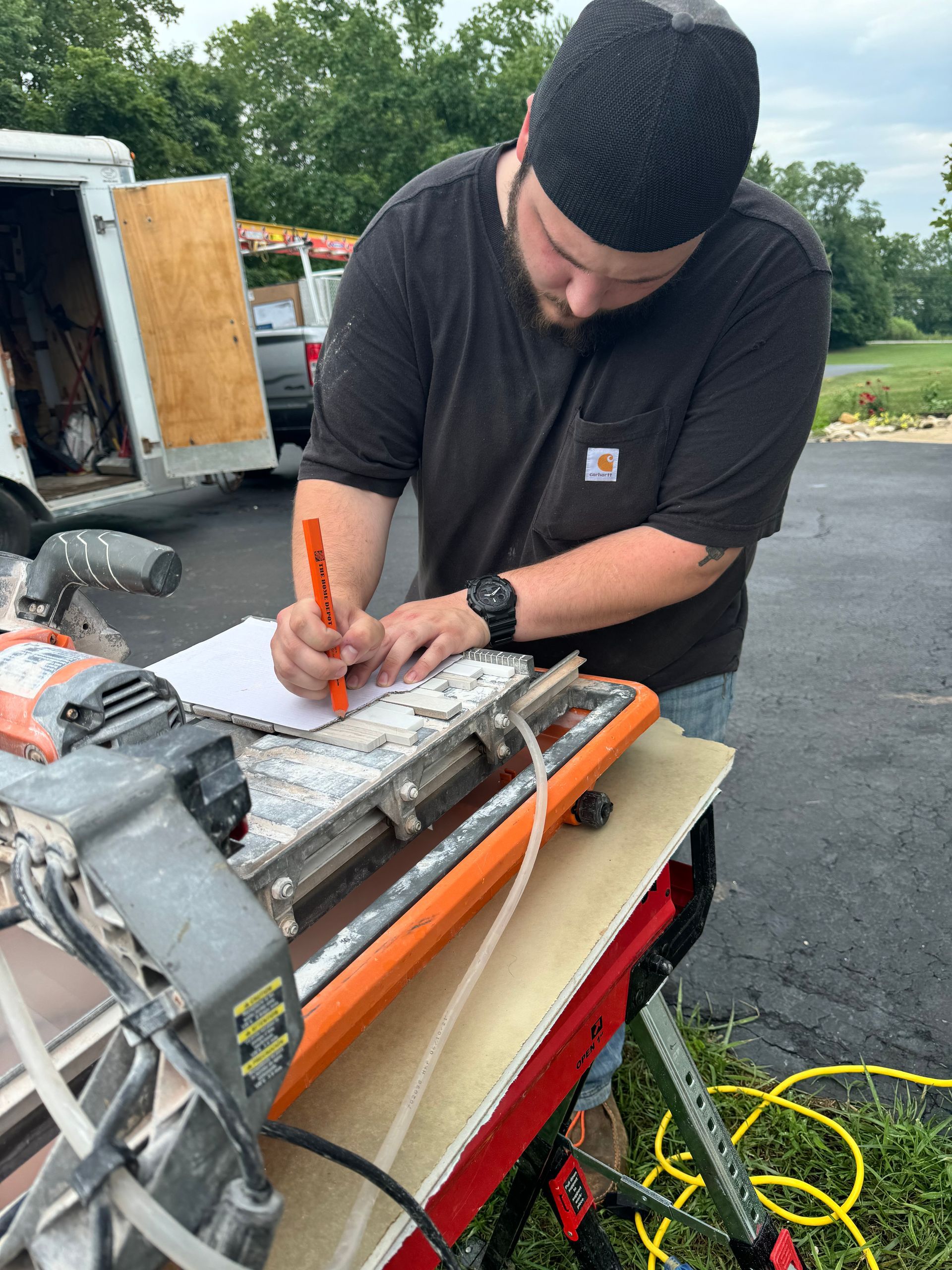 Man using a utility knife to cut material on a workbench outdoors, with tools and cables nearby