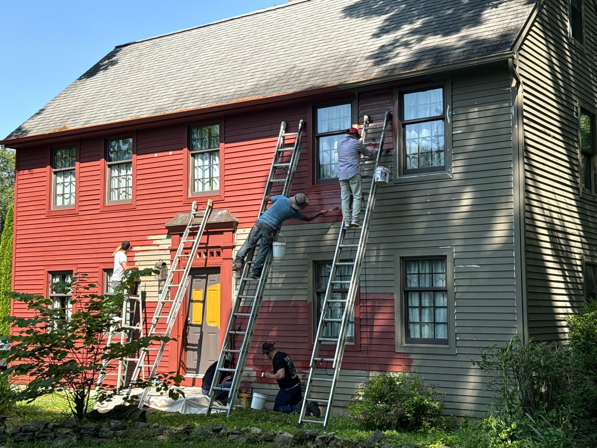 Workers on ladders painting the exterior of a red and green house