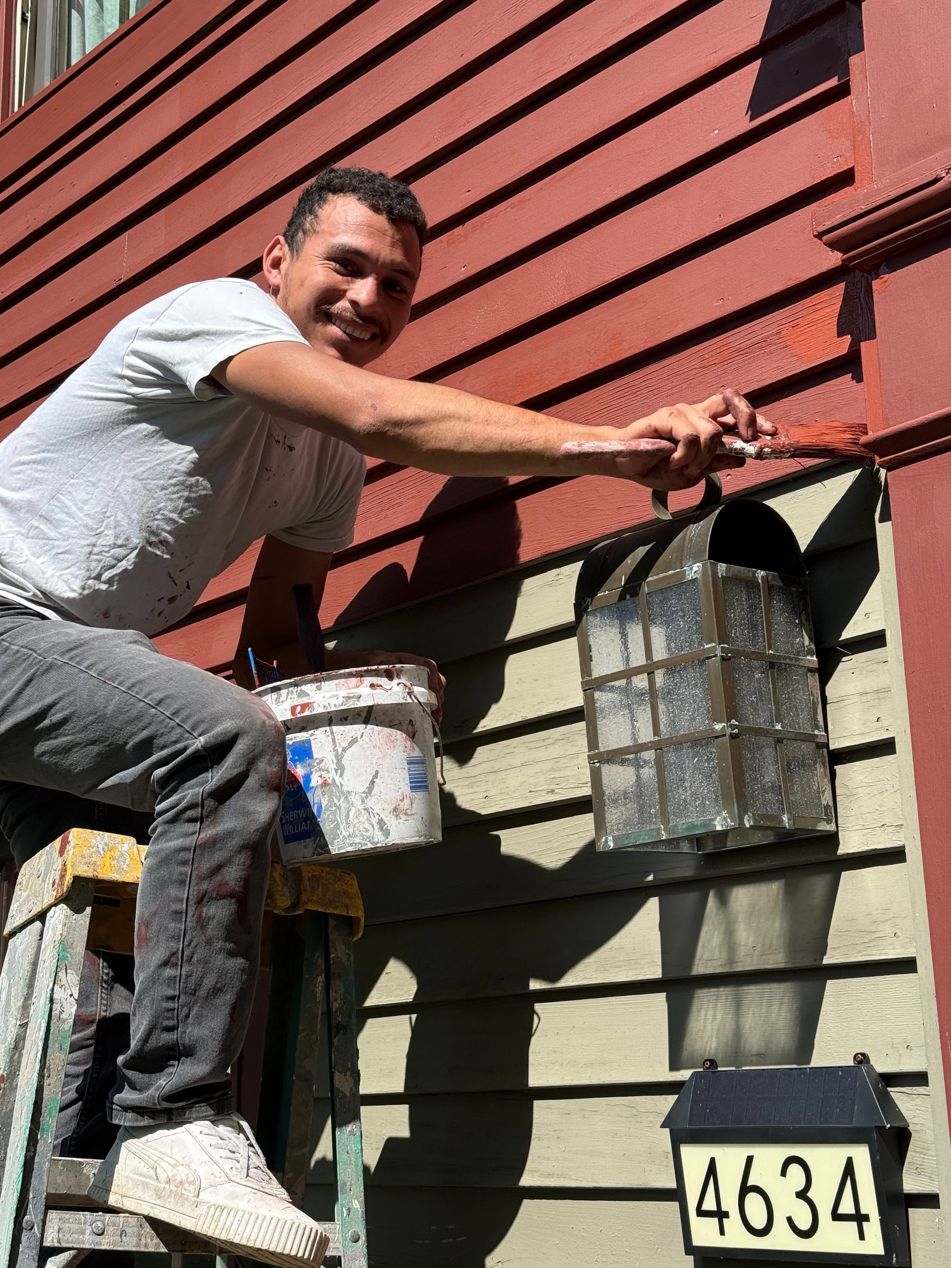 Person installing a wall-mounted lantern beside house number 4634 on a red and green exterior wall