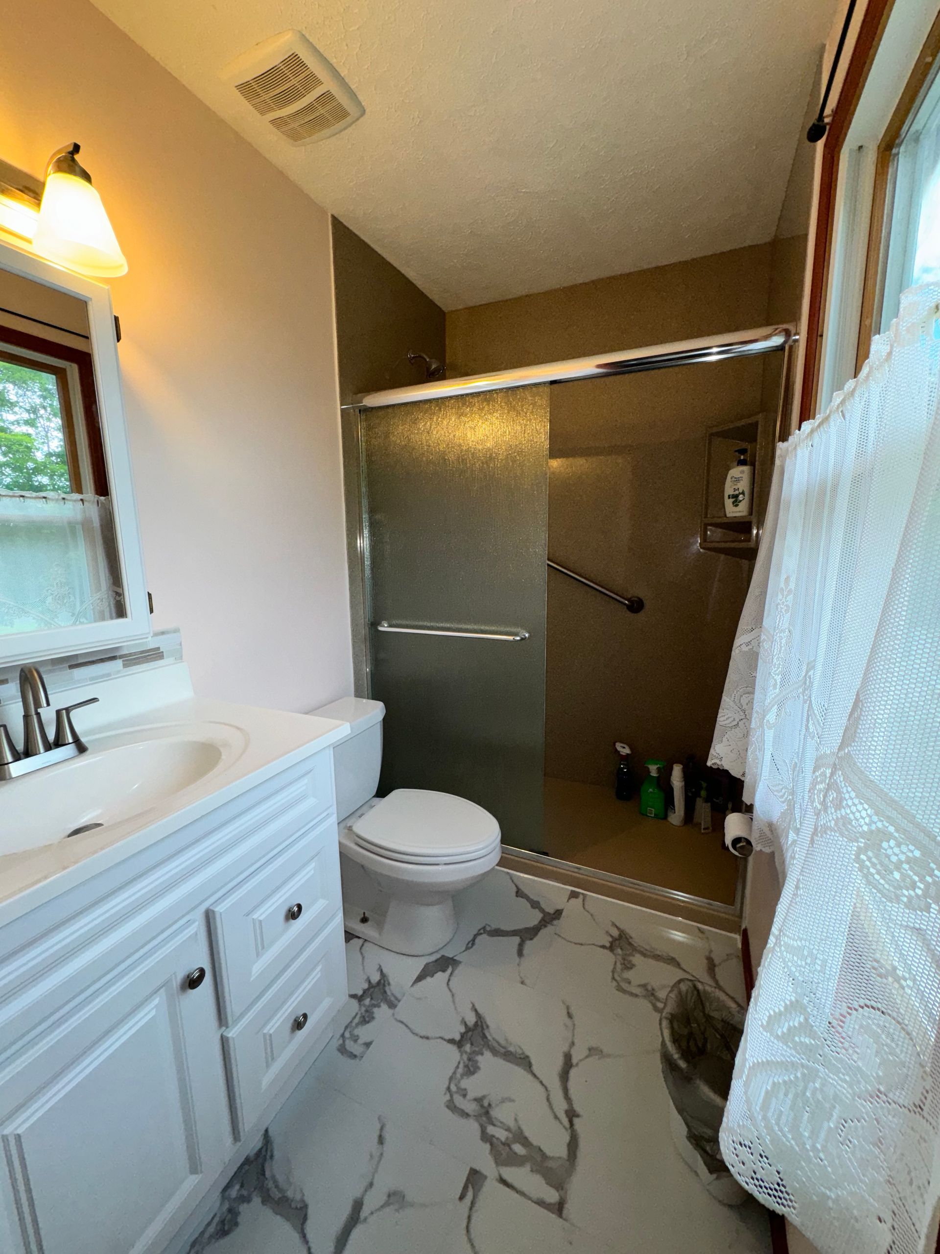 Small bathroom with white vanity, toilet, glass shower, and marble-pattern tile floor.