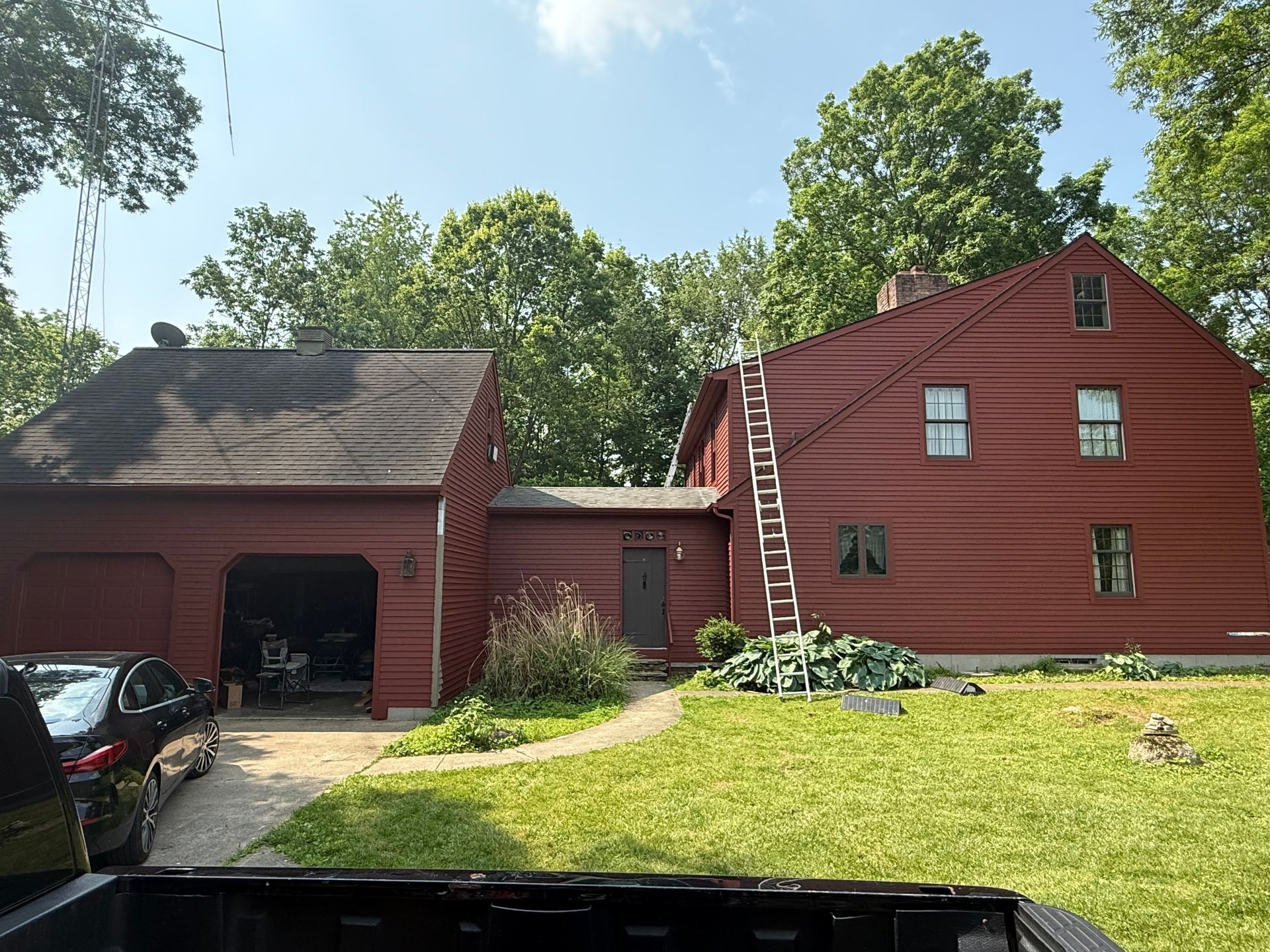 Red house with attached garage, parked car, and green lawn under trees on a sunny day