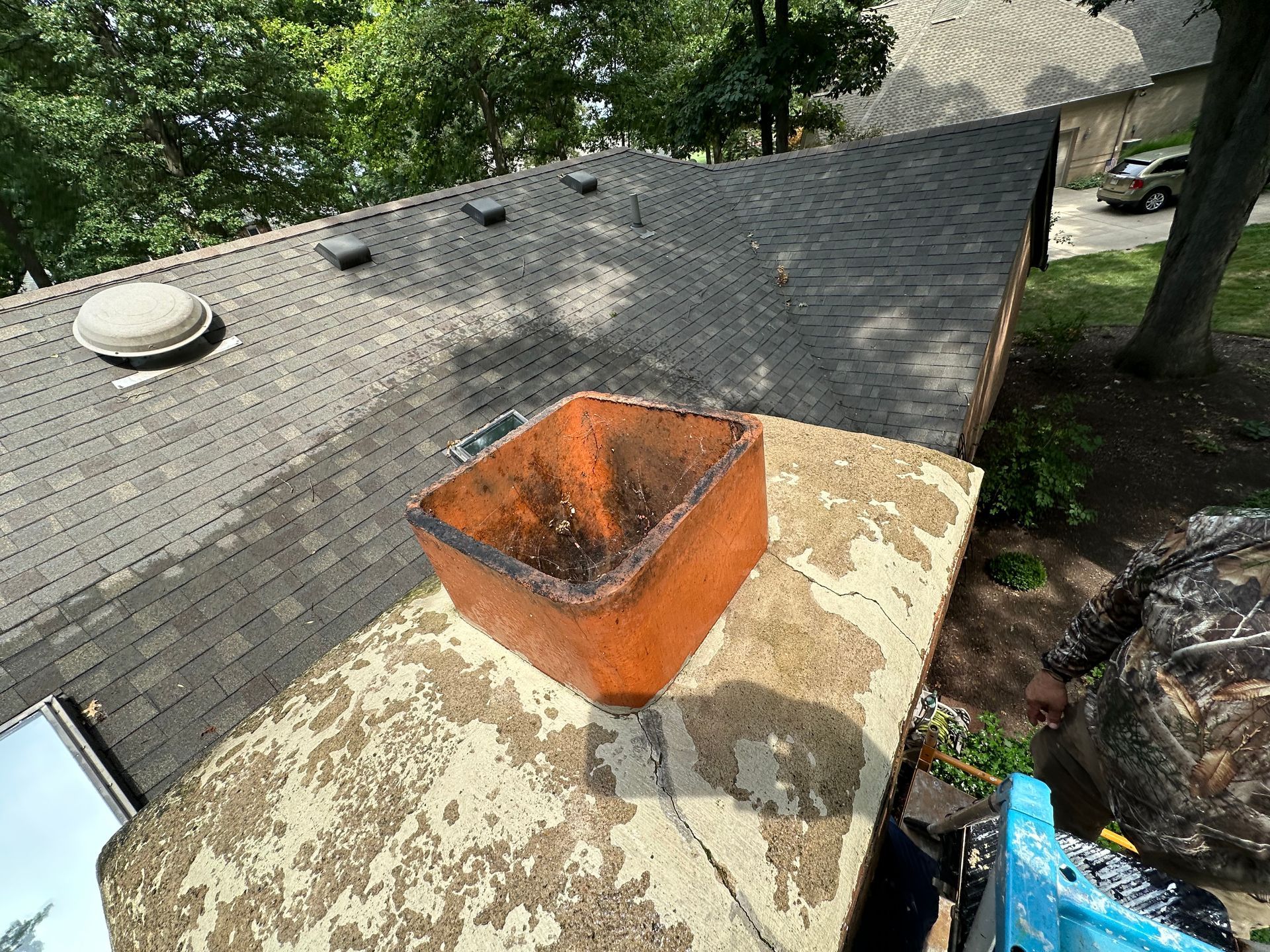 Orange chimney vent on a shingled roof with moss stains, seen from above.