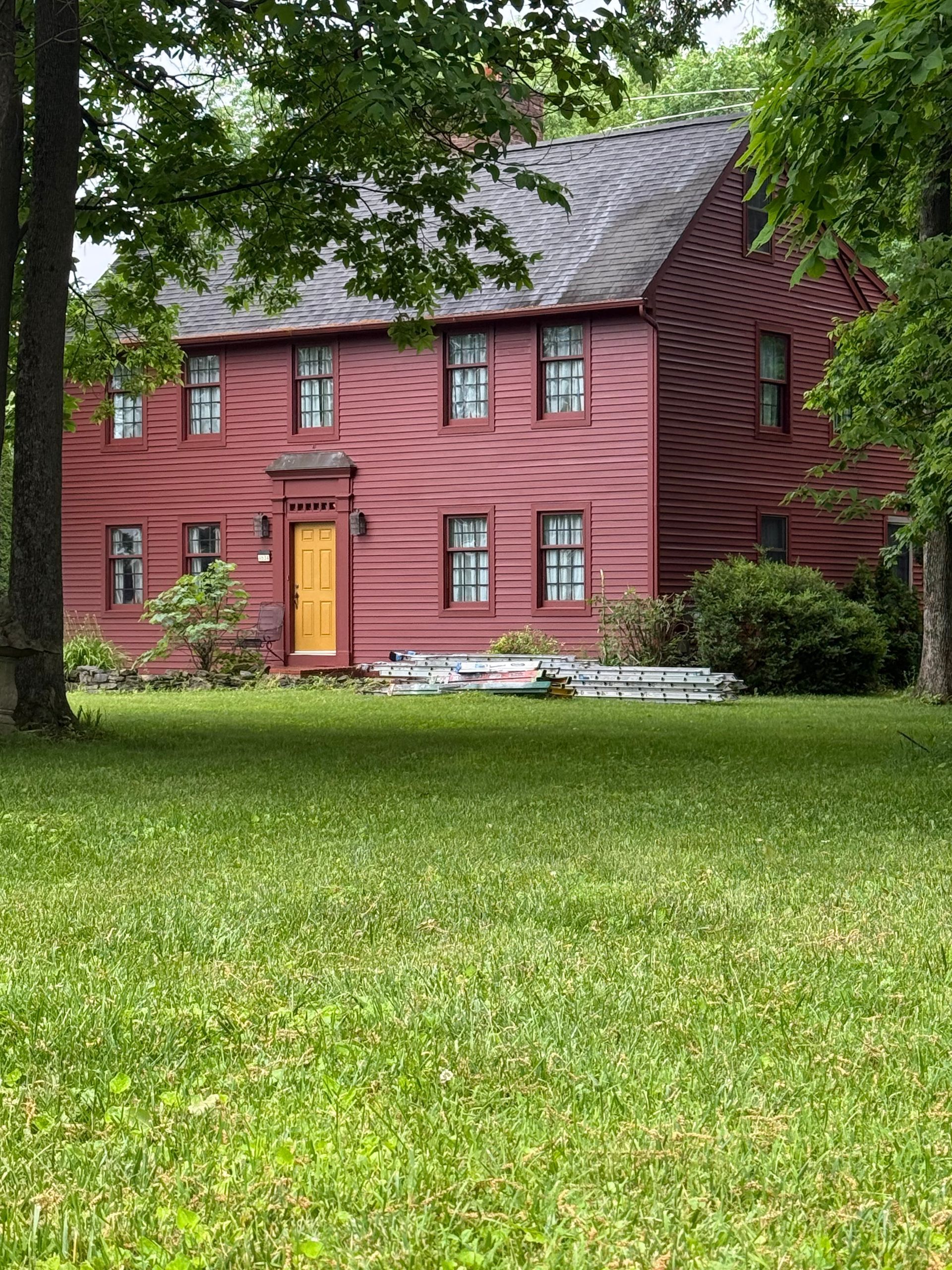Red two-story house with yellow door, set behind a green lawn and framed by trees.