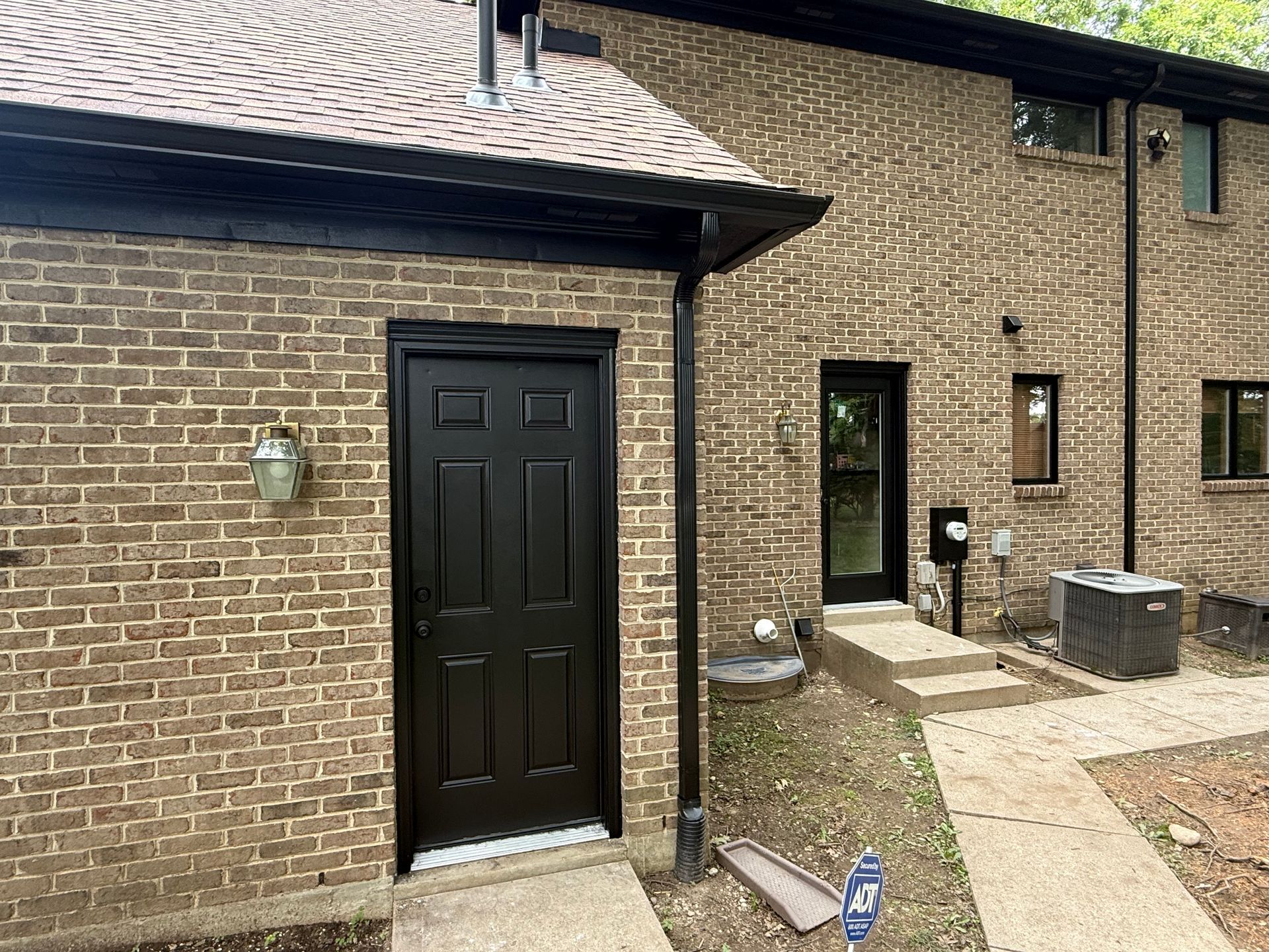 Brick building exterior with black door, narrow windows, and a small paved walkway.