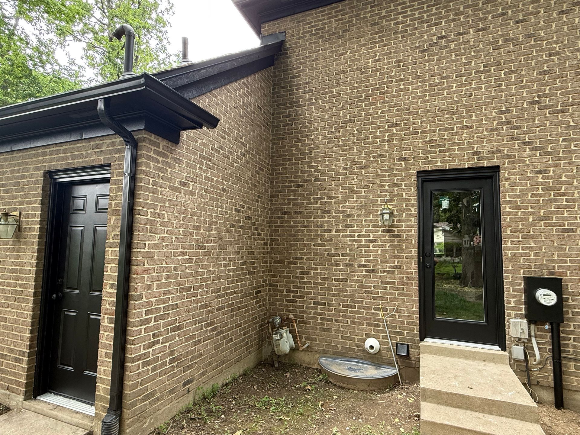 Brick house exterior with a black front door, window, and small concrete steps near a side entrance.