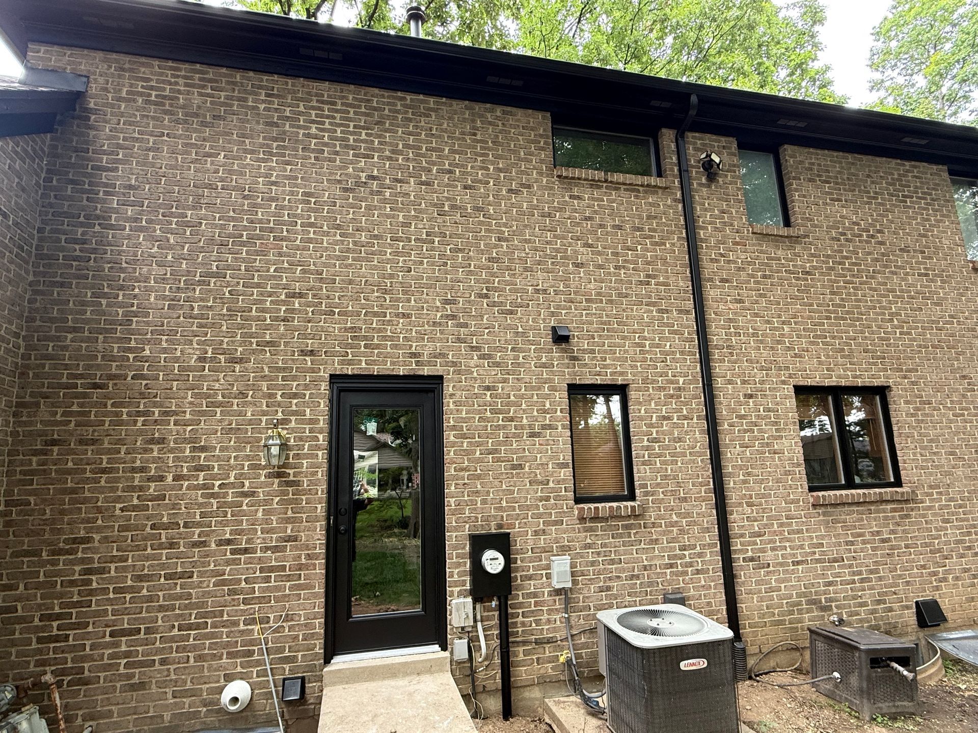 Brick house exterior with black door, small windows, and outdoor sink in a wooded setting