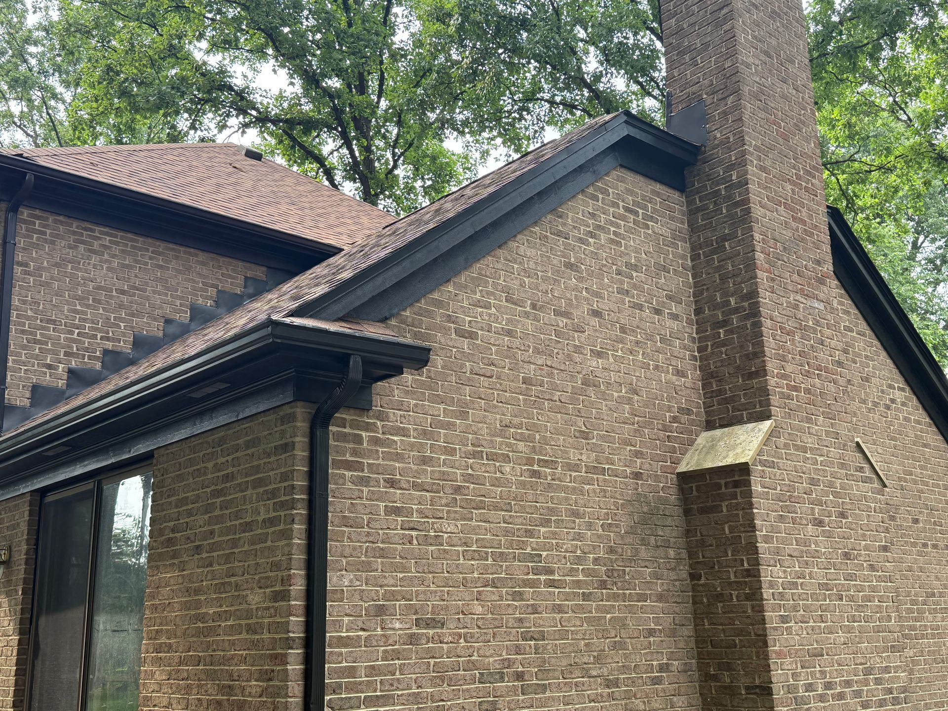 Brick house exterior with steep roof, chimney, and trees in the background