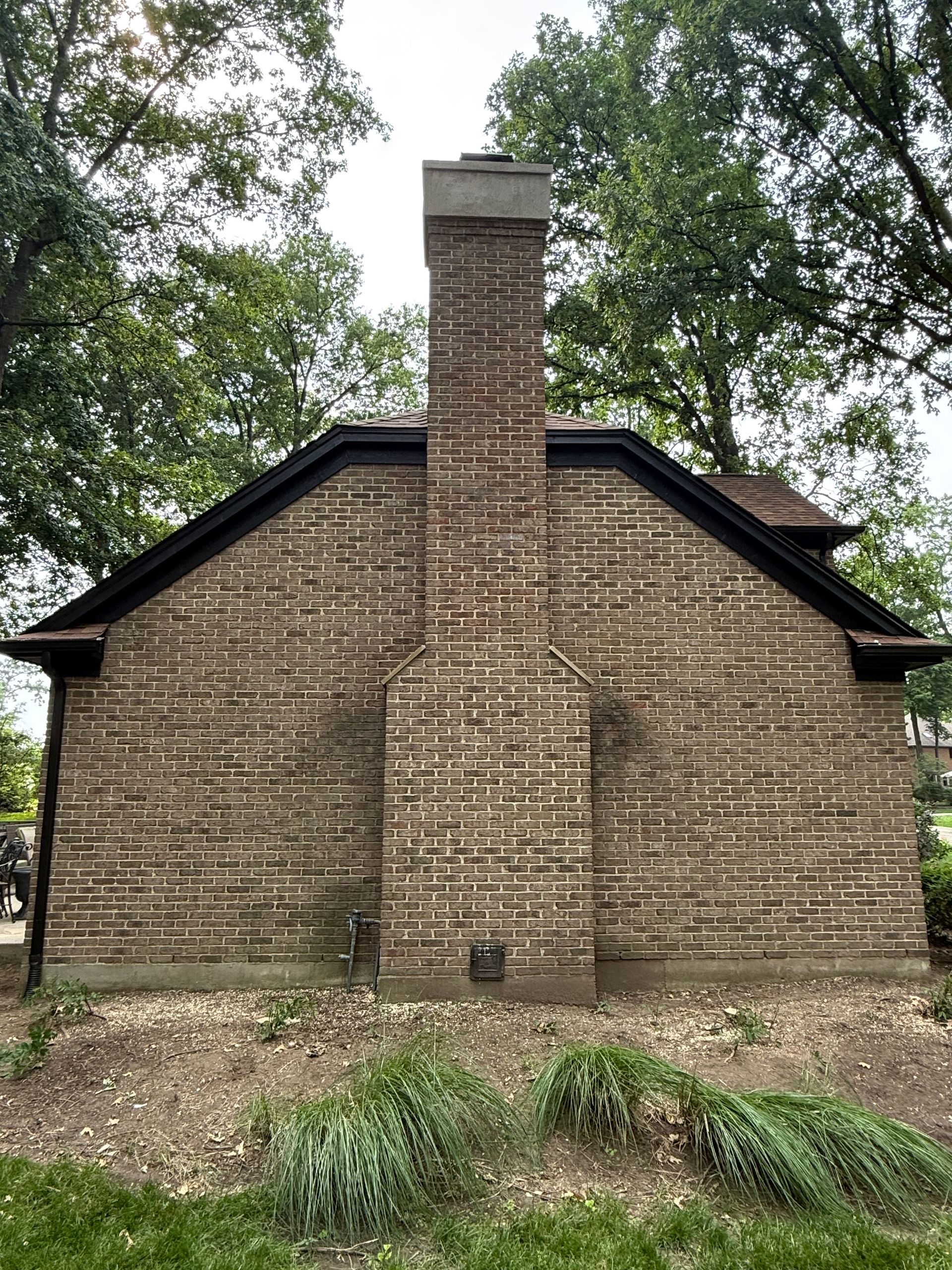 Brick chimney centered on a small wooden building, surrounded by trees and grass.