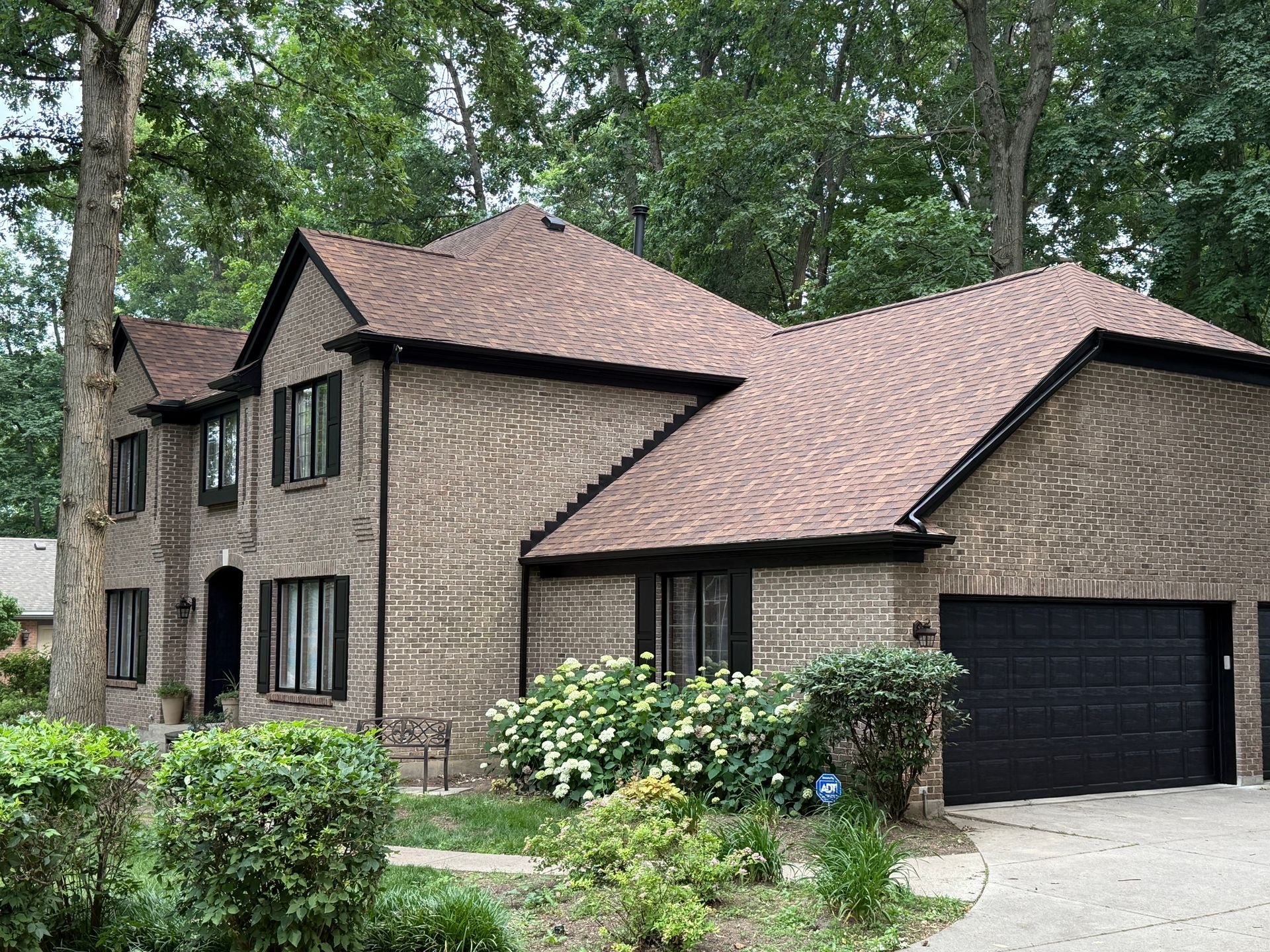Brown two-story house with black garage and wooded yard