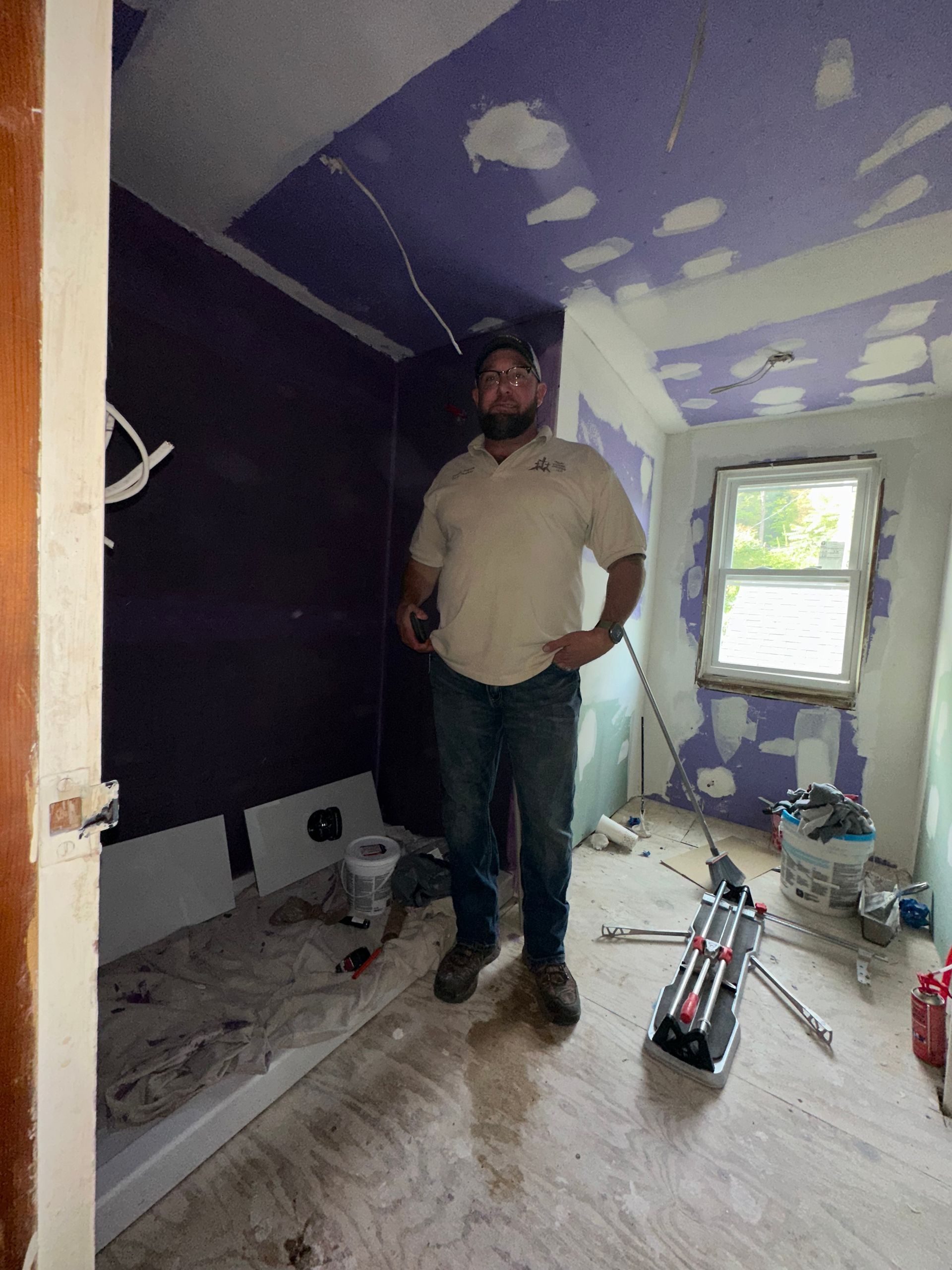 Person standing in a small room under renovation with purple drywall patches and tools on the floor