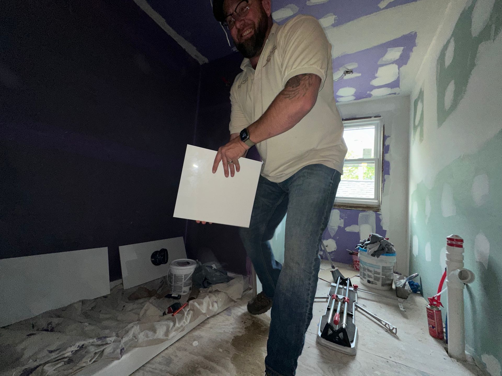 Person standing in a room under renovation, holding a white panel amid construction tools and debris.