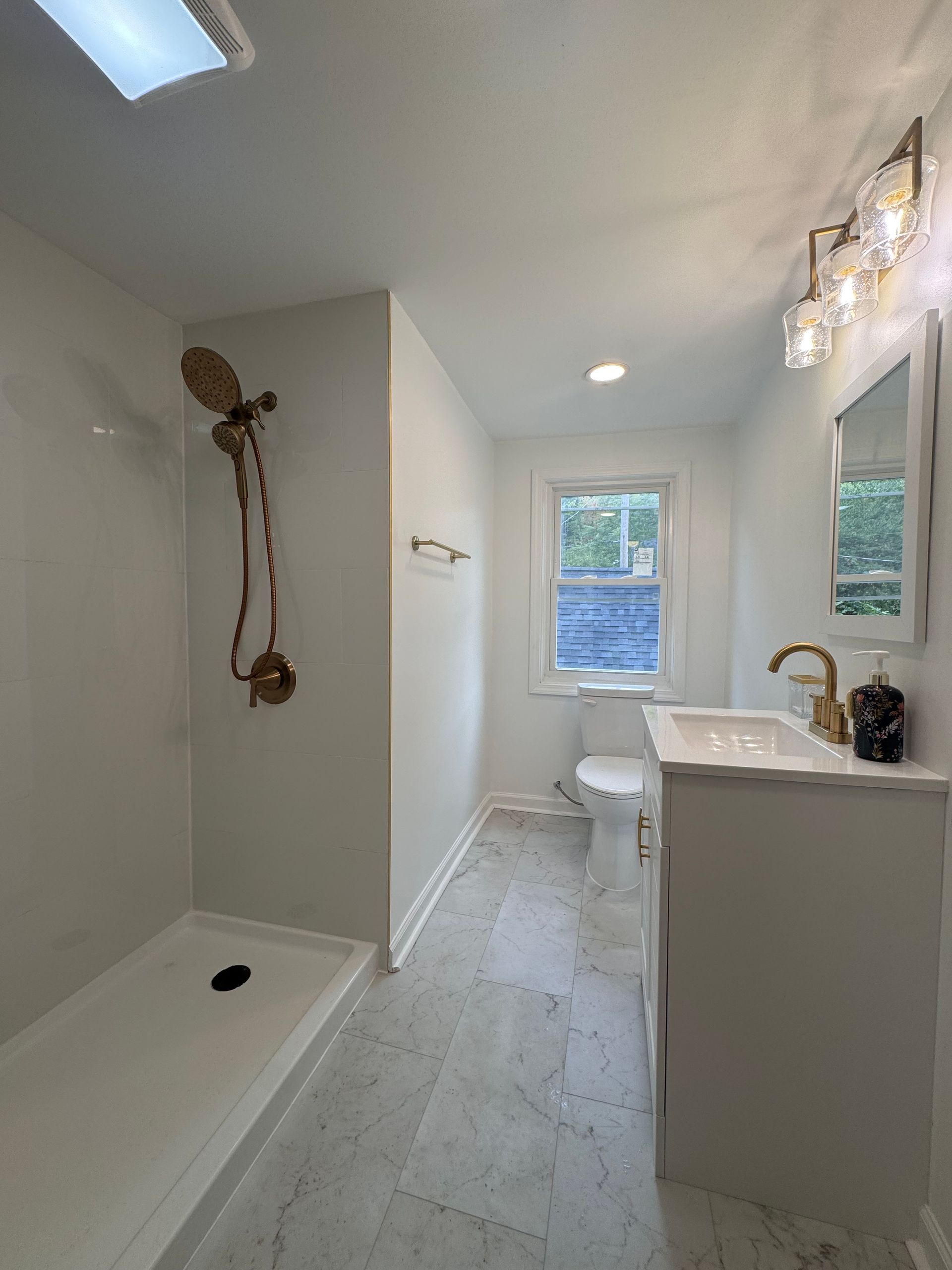Modern white bathroom with walk-in shower, vanity, toilet, and window at the end.