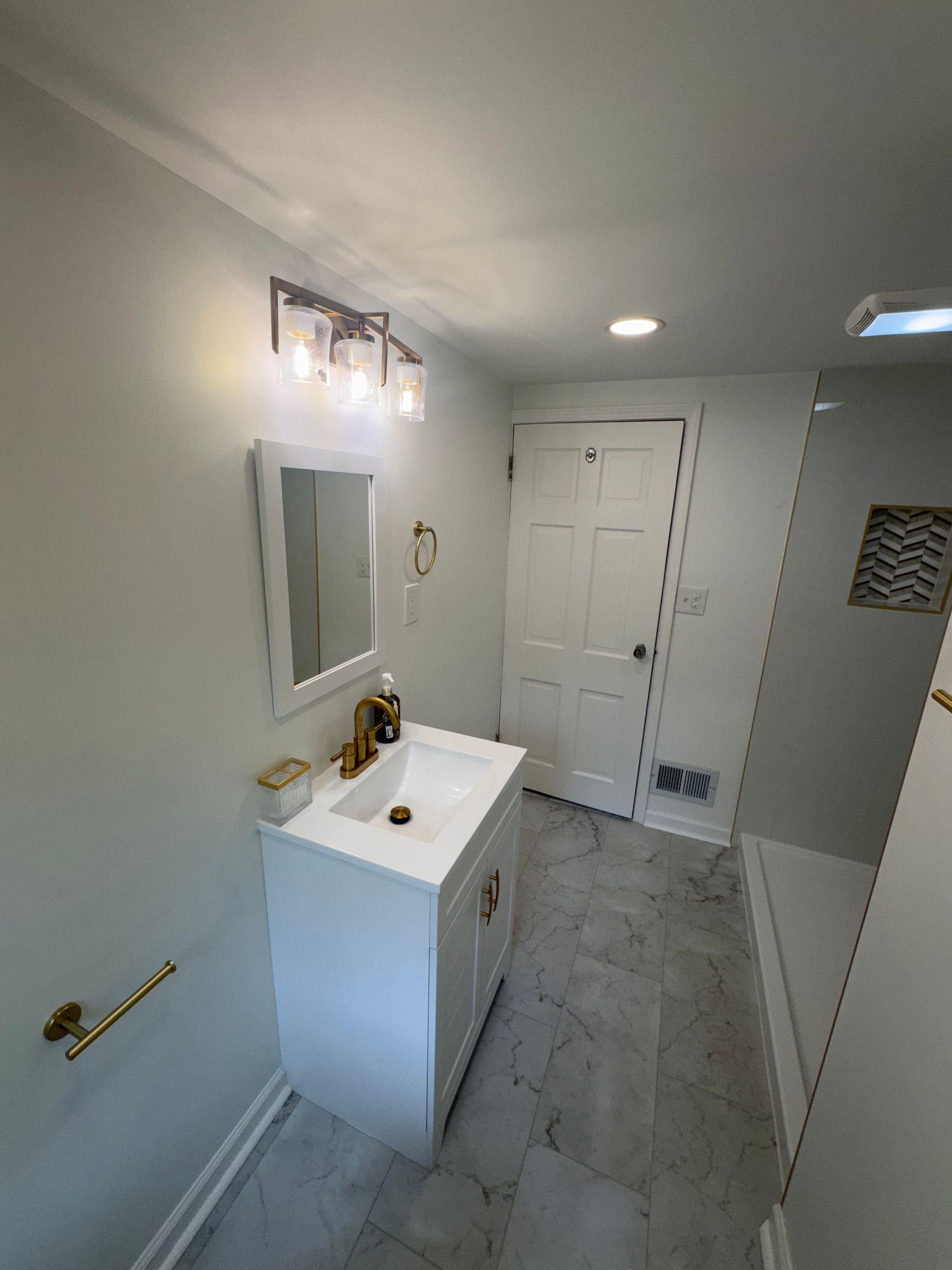 Narrow white bathroom with vanity, mirror, towel bar, shower, and closed closet doors.