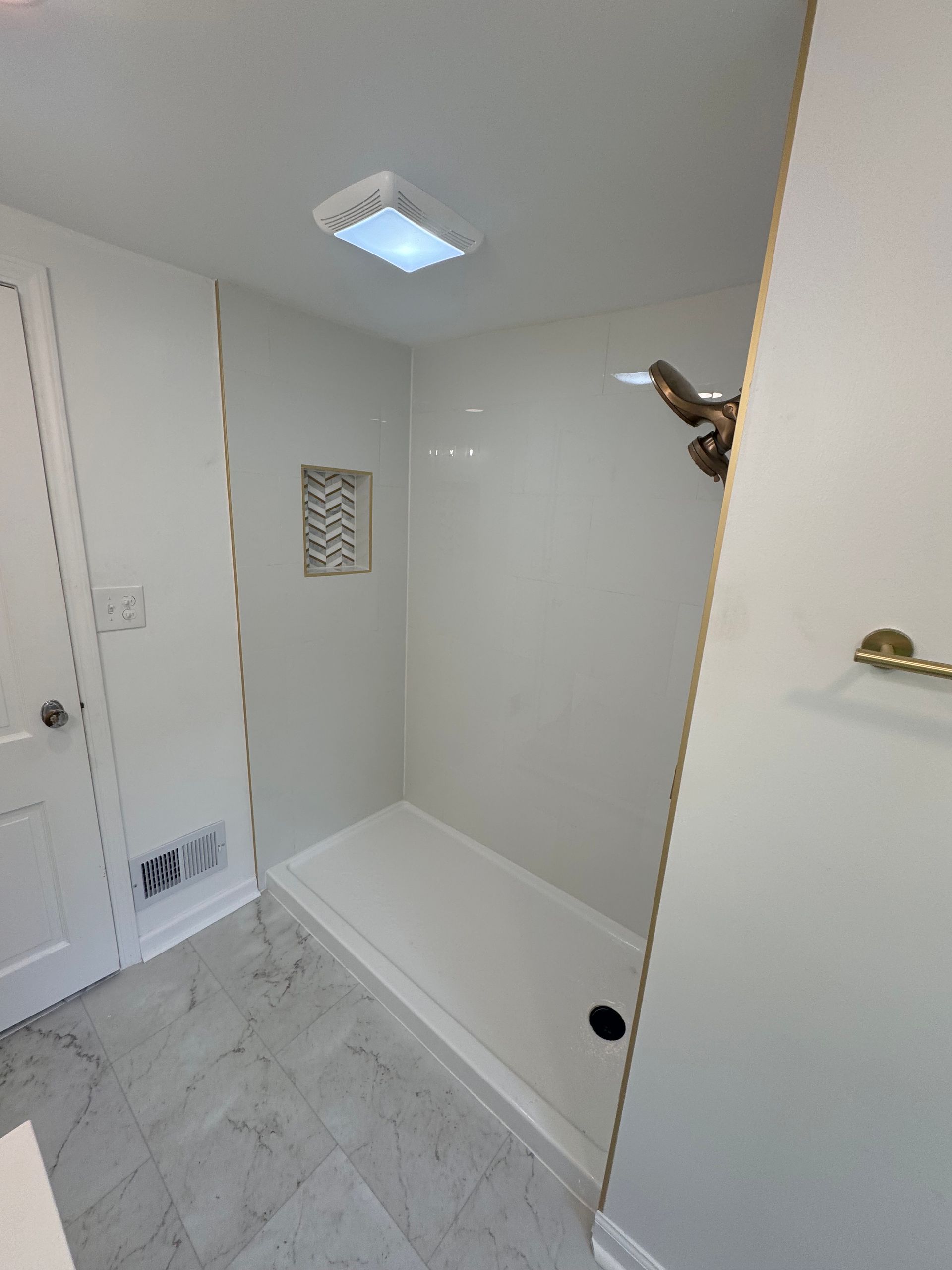 Empty white shower stall with bench, grab bar, and skylight in a bathroom