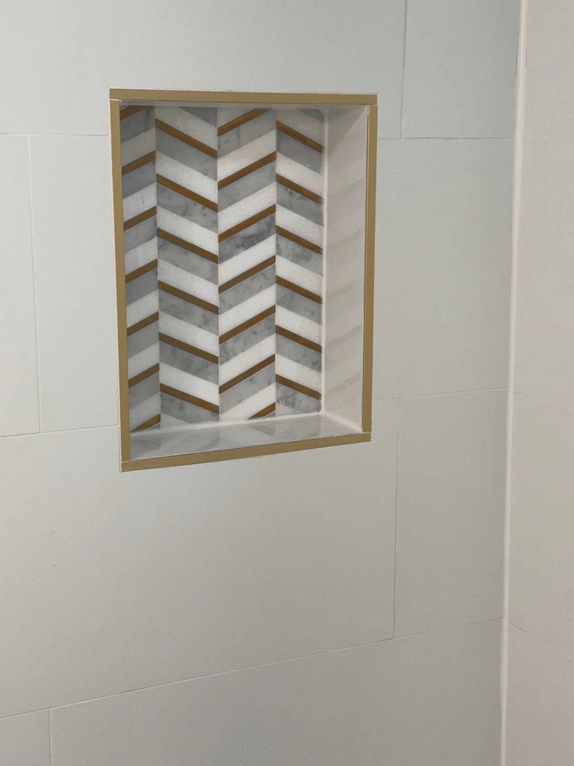 Small recessed wall niche with a geometric chevron tile pattern in beige, gray, and white.