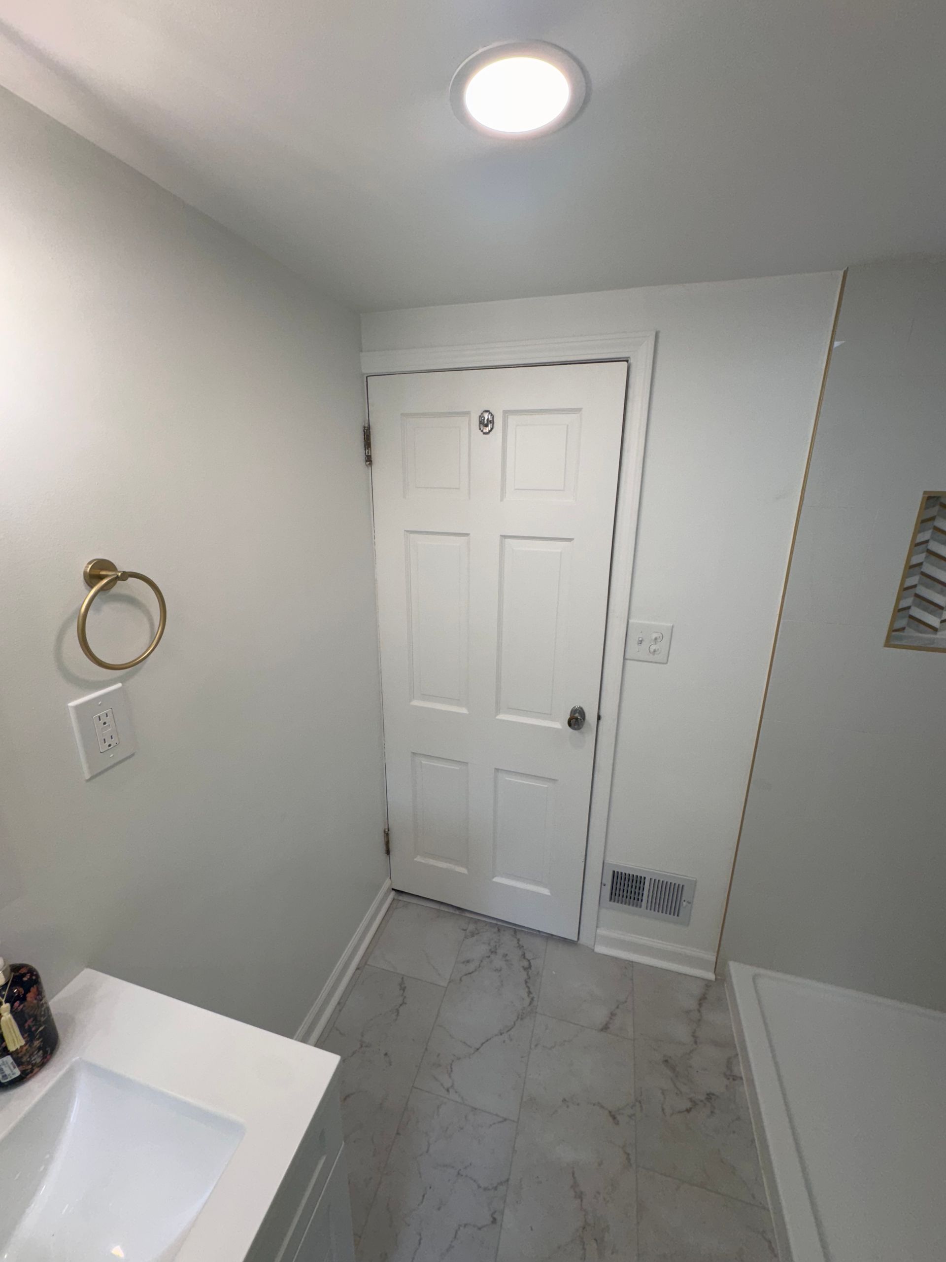 Small white bathroom with a sink, toilet door, and marble-pattern tile floor.