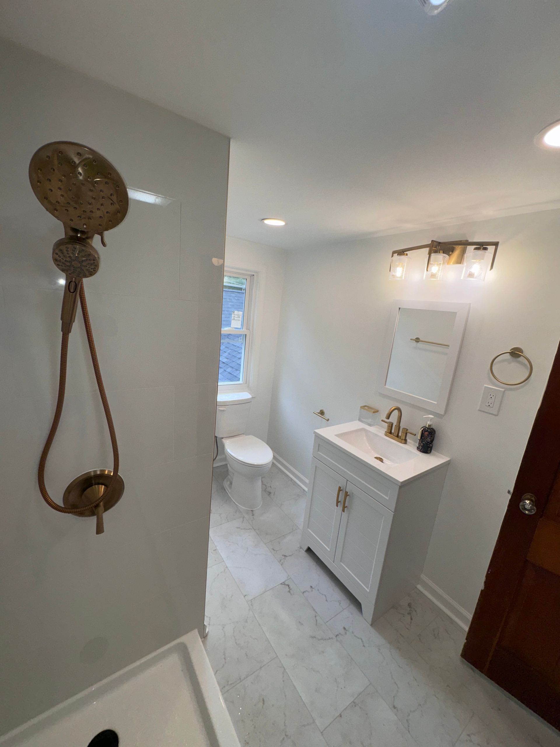Small bathroom with white vanity, mirror, toilet, wall sconce, and hanging shower loofah.