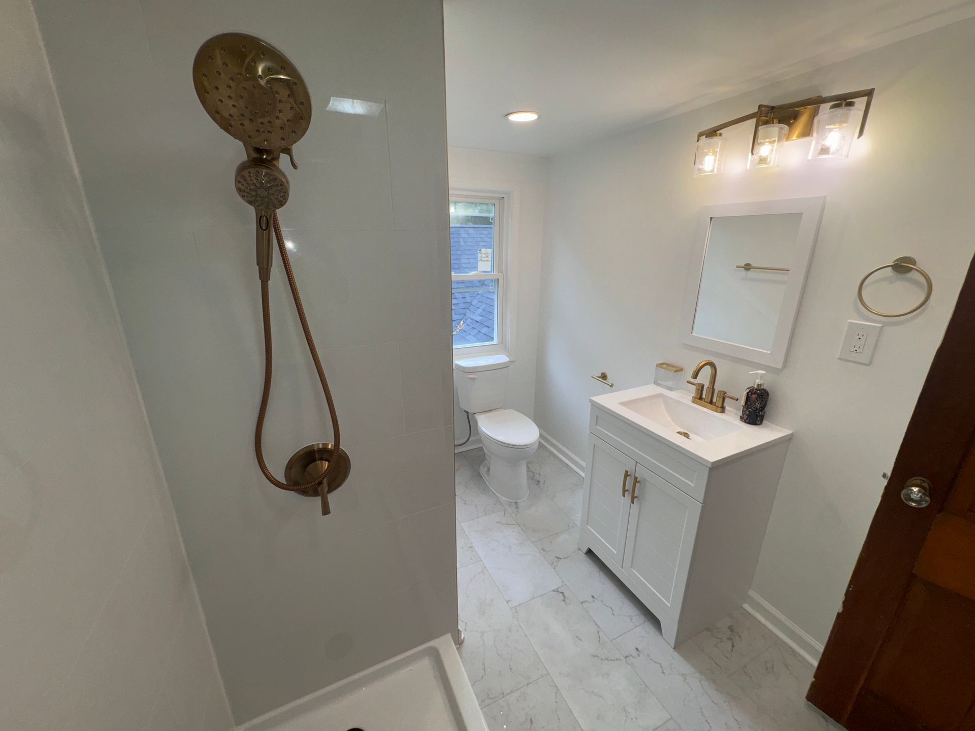 Bright bathroom with white vanity, toilet, window, and bronze shower fixture on the left wall.