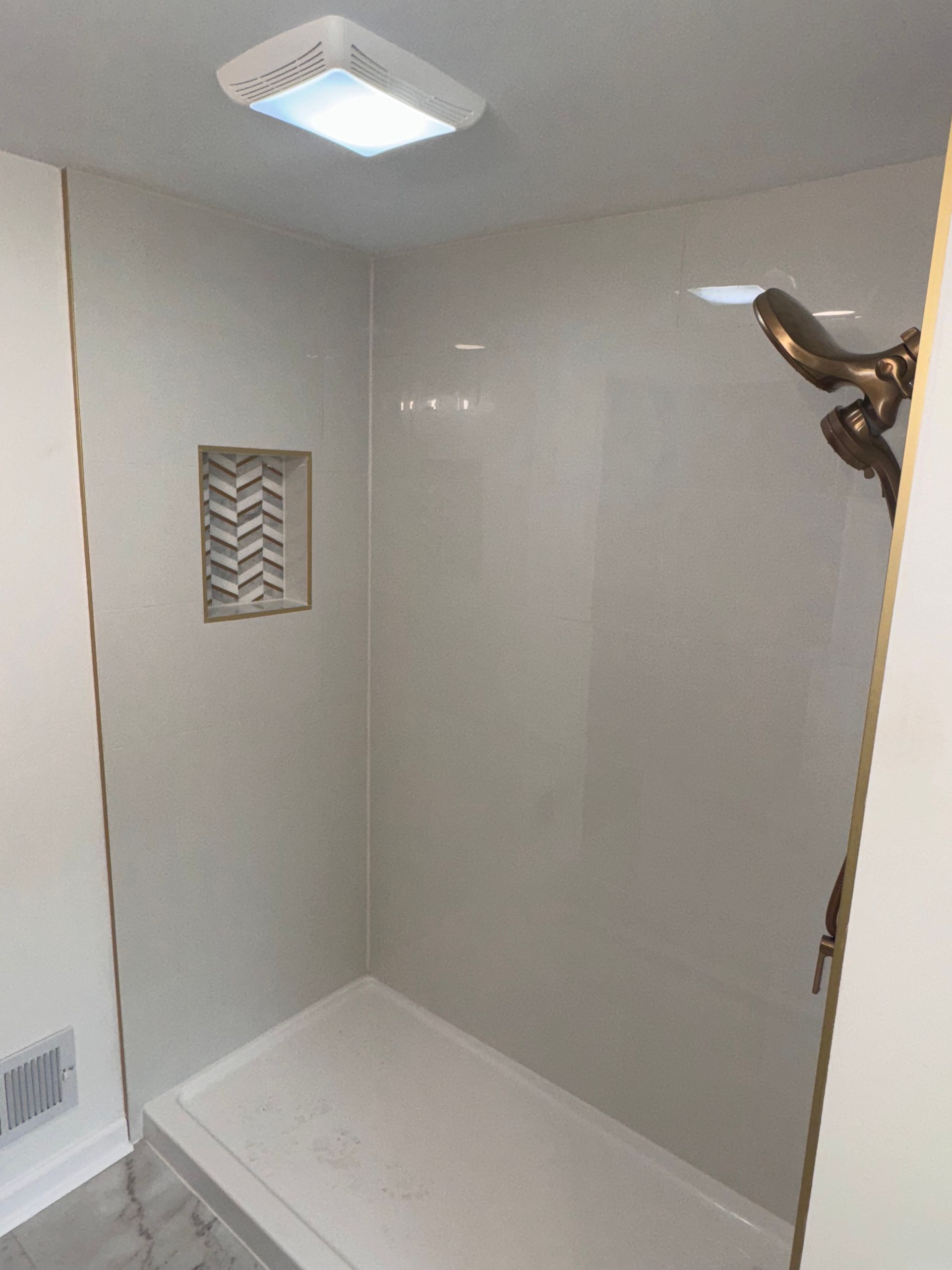 Empty tiled shower stall with white walls, built-in shelf, and grab bar on the right.