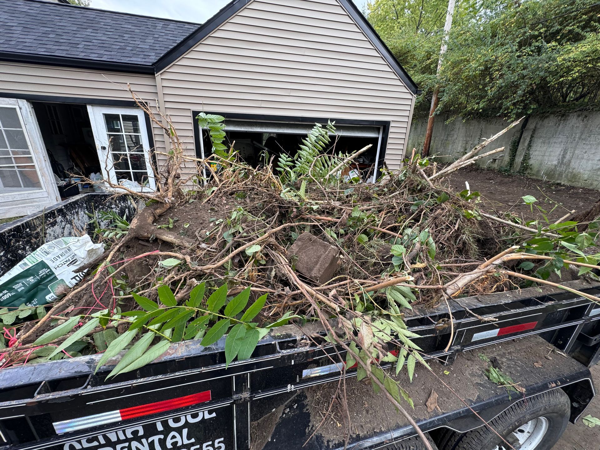 Truck bed piled with yard debris and branches in front of a house and garage